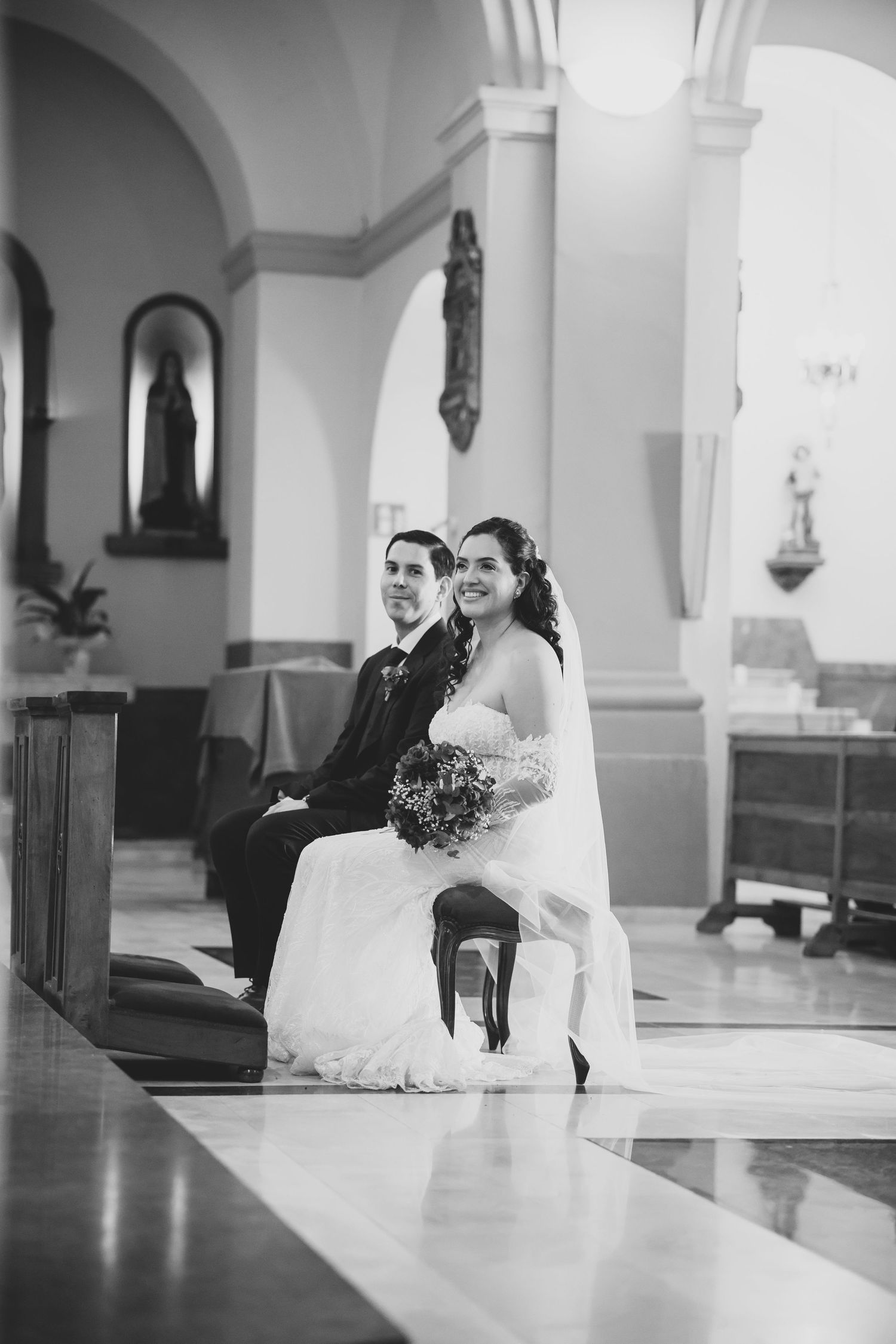 Black and white photo of a smiling bride and groom seated together during a church wedding ceremony.