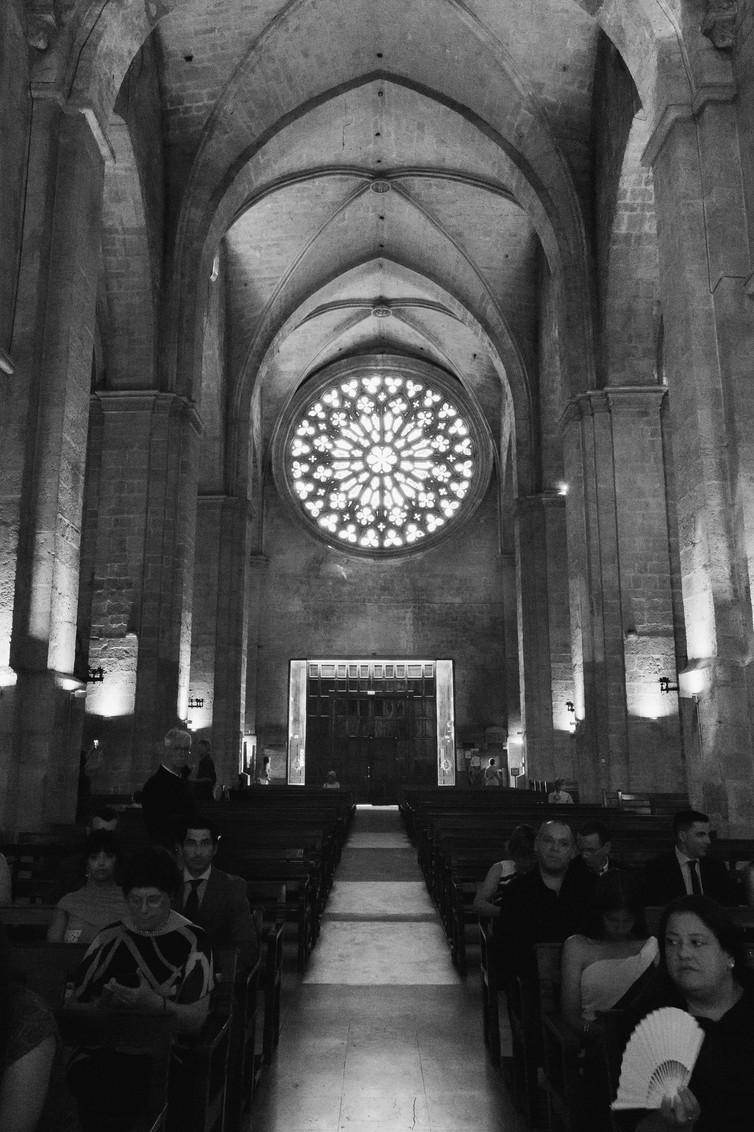 Black and white interior of Gothic cathedral with rose window, vaulted arches, and wedding guests in pews.