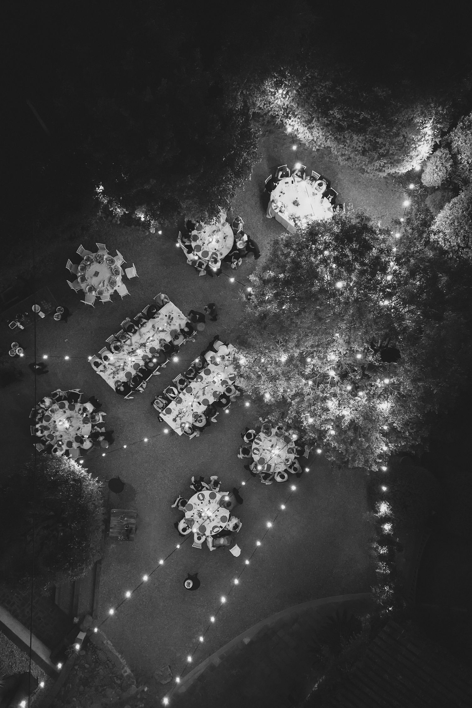 Aerial black and white night view of illuminated outdoor wedding reception tables and guests.