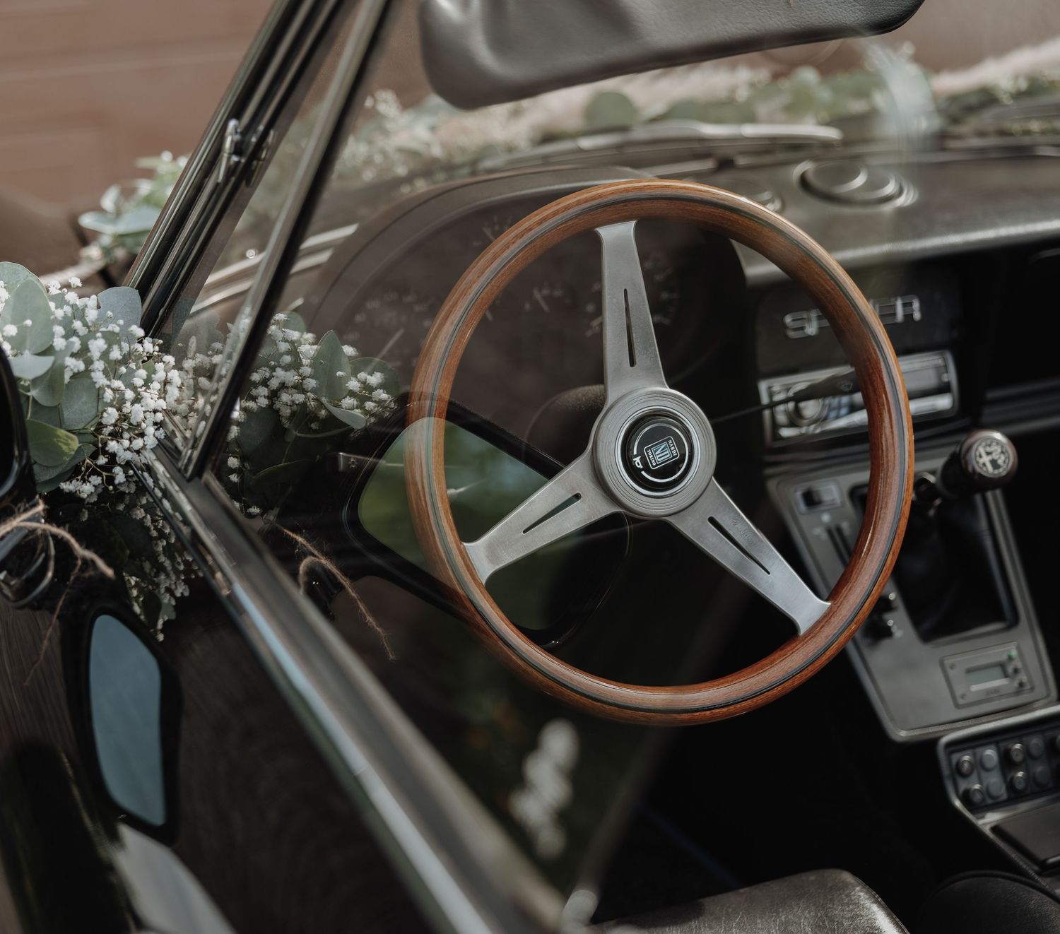 Classic vintage black car decorated with wedding flowers featuring a wooden Nardi steering wheel.