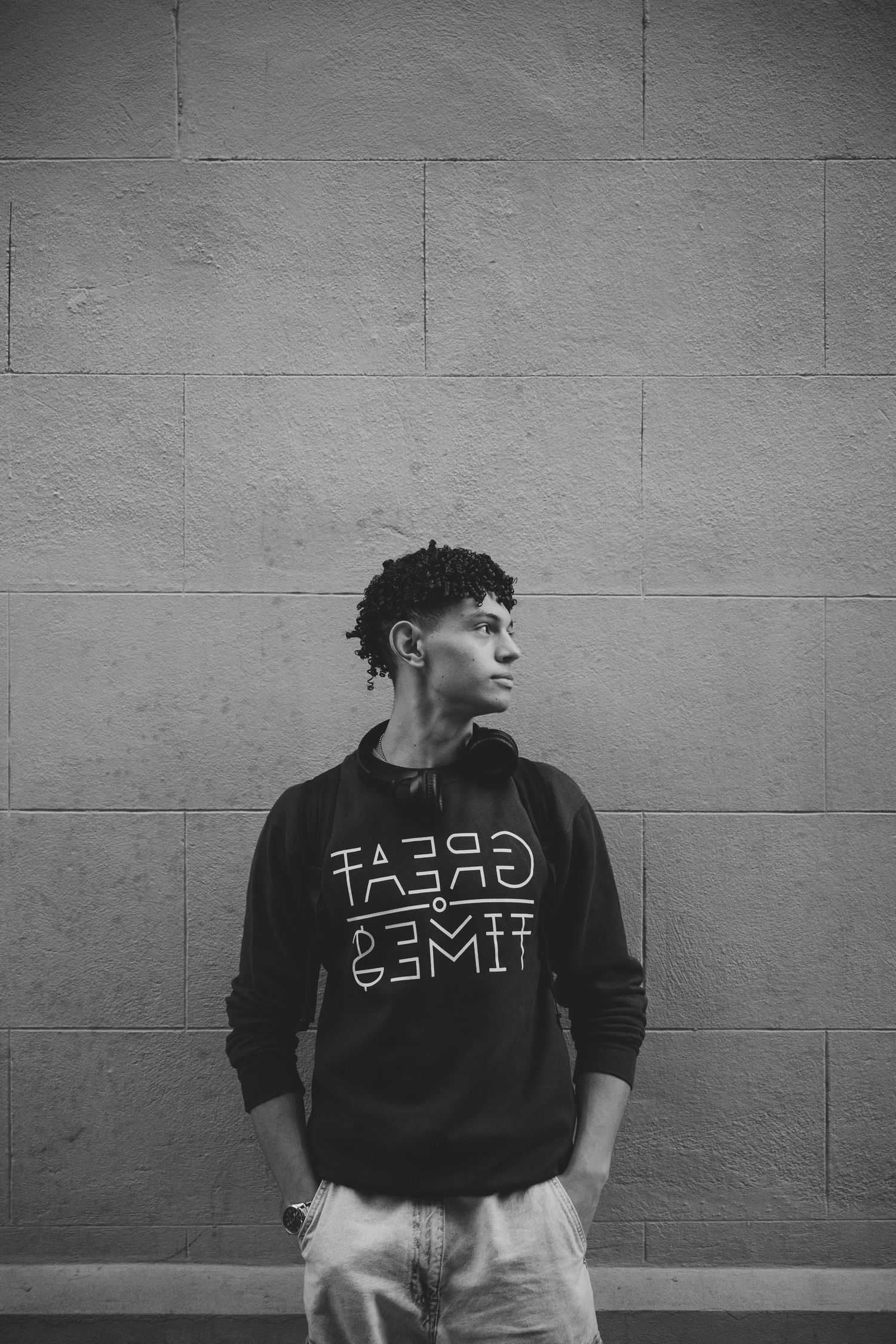 Black and white portrait of a young man in a graphic sweatshirt leaning against a concrete wall.