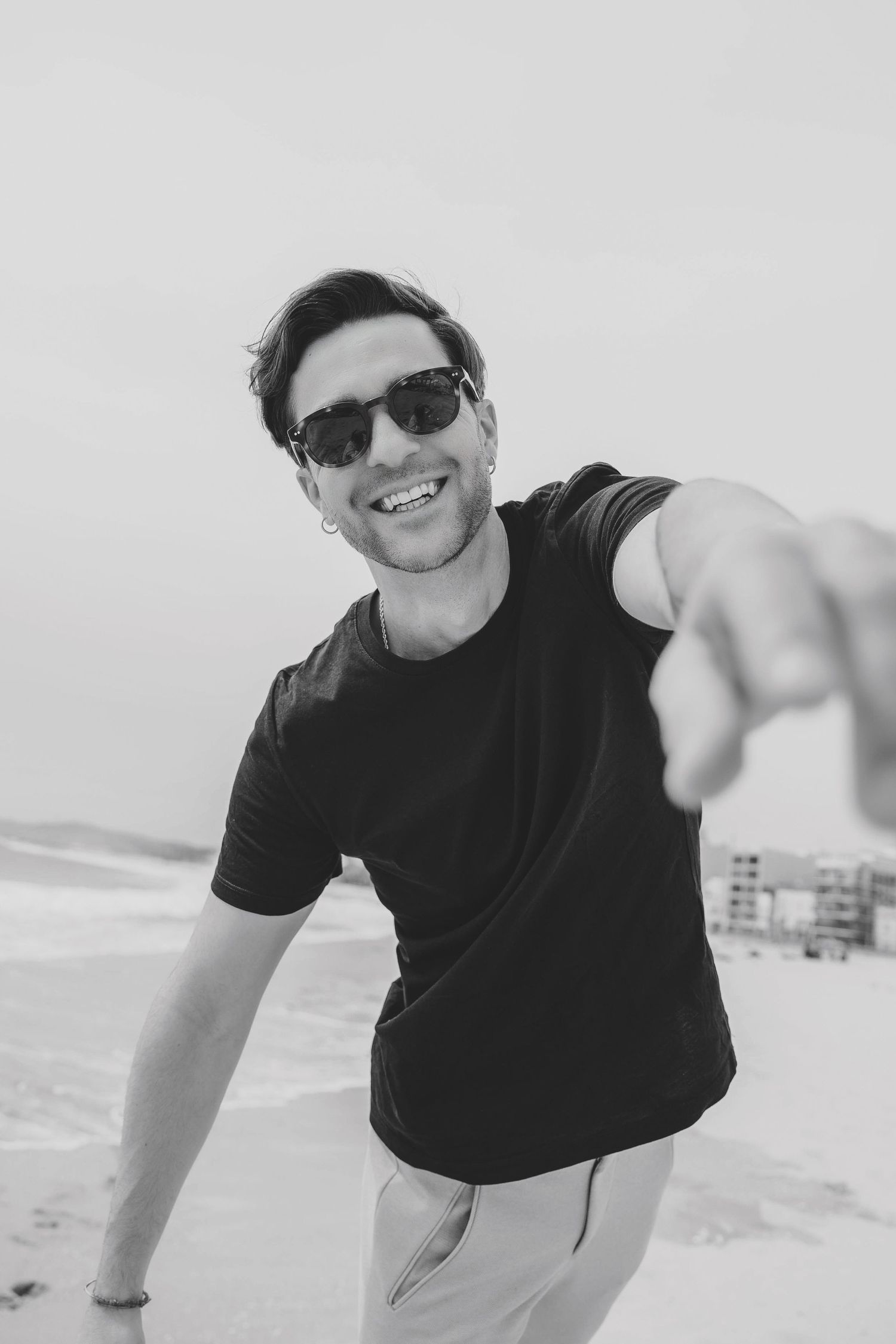 Smiling man in sunglasses taking selfie on beach.