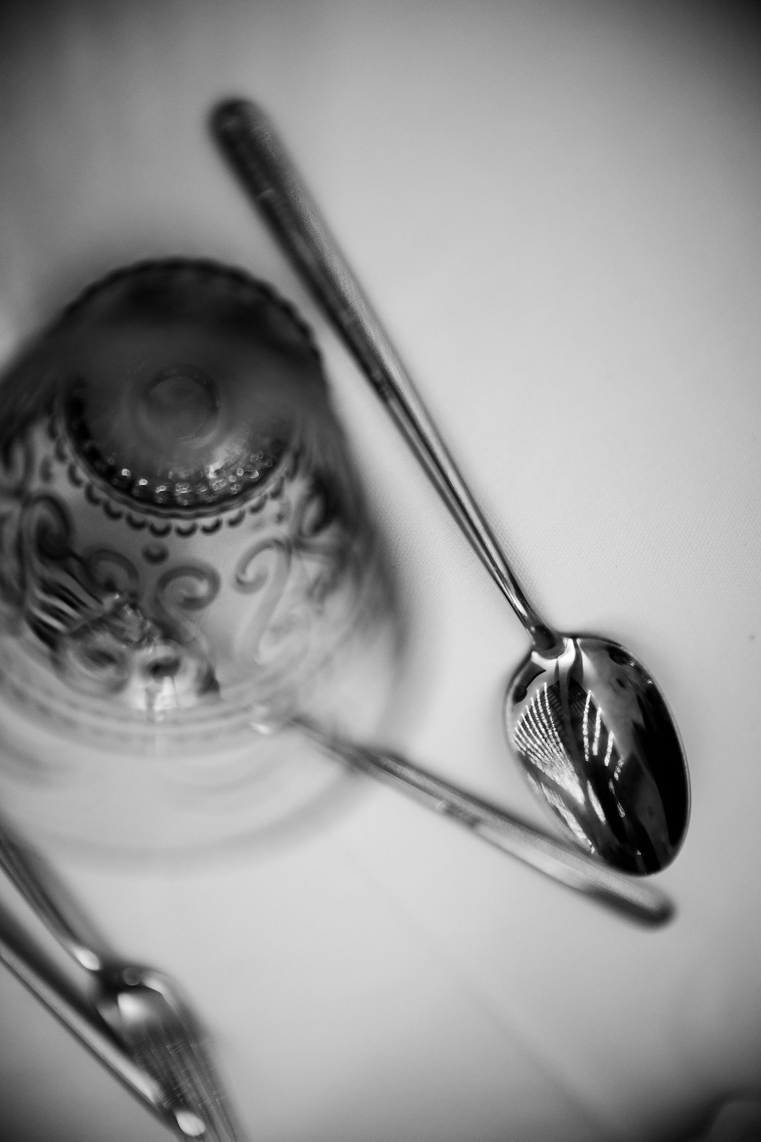 Black and white close-up of ornate crystal glass and decorative silver spoon on white surface.