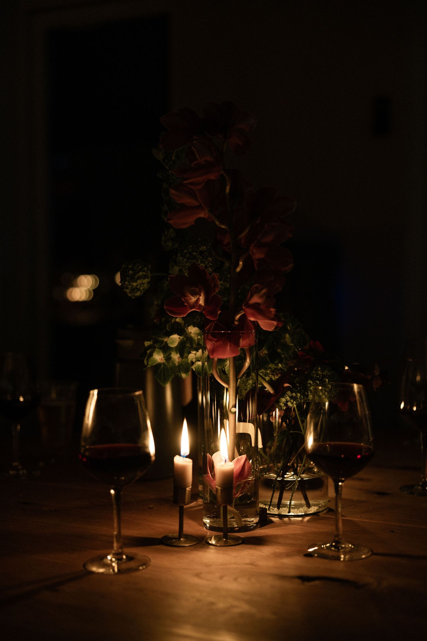 Romantic candlelit dinner table with red wine glasses and floral centerpiece in dark ambiance.