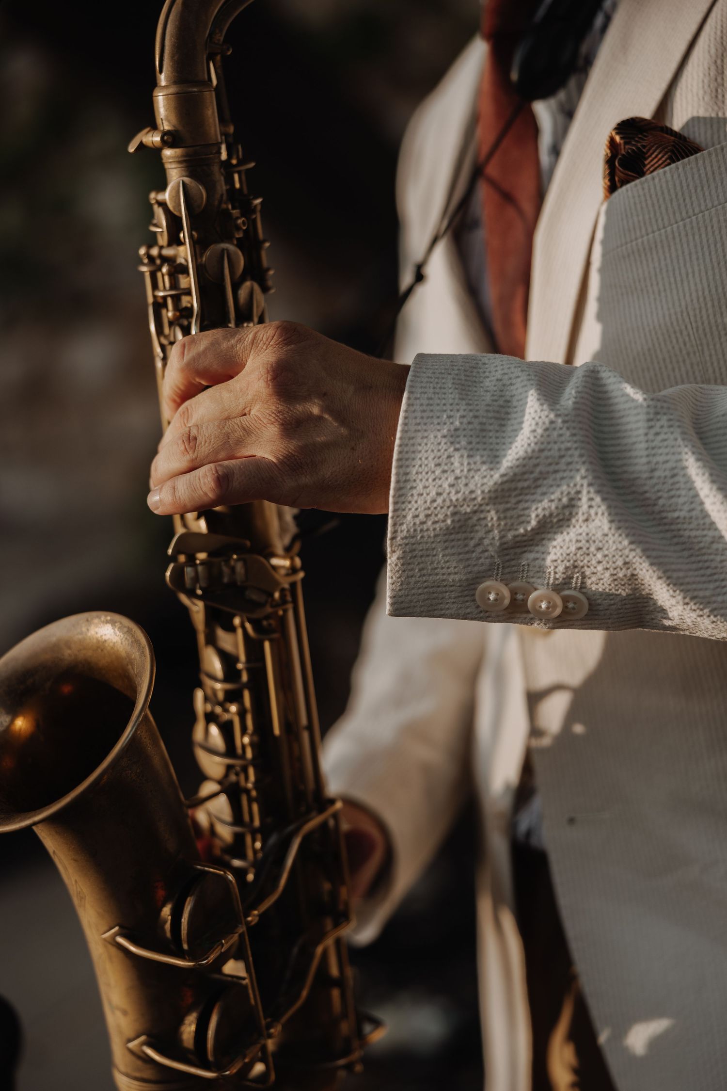 Close-up of a musician in a white suit playing a vintage brass saxophone at a wedding reception.