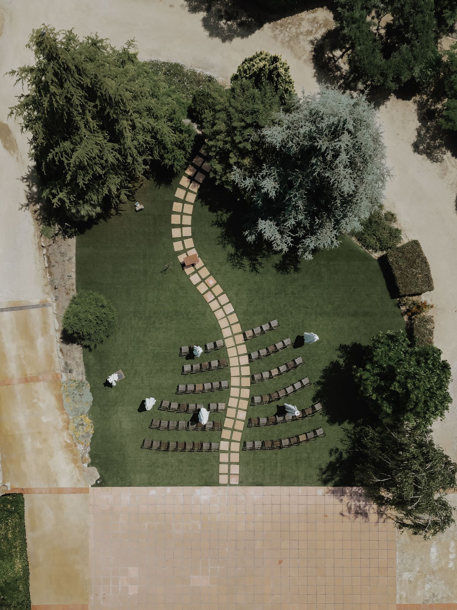 Aerial view of an outdoor wedding ceremony setup with chairs arranged on green lawn and winding brick path.