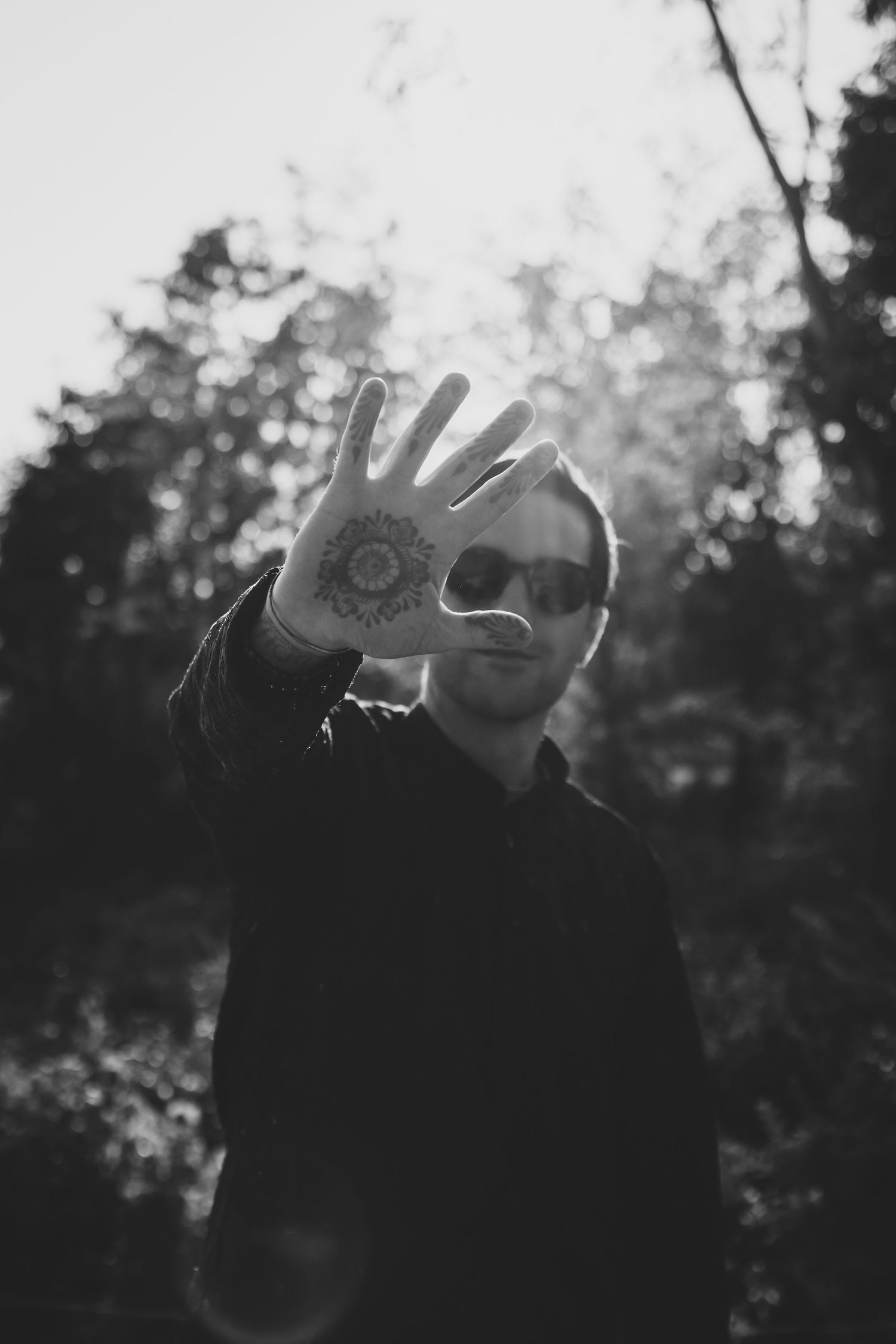 Man holding tattooed hand up in forest setting.