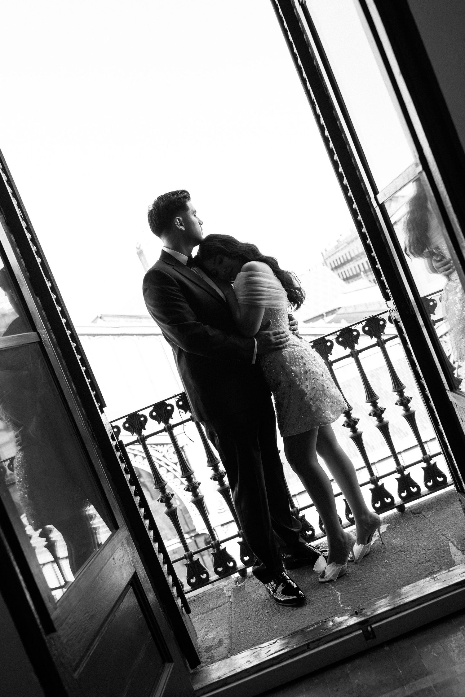 Black and white silhouette of a couple embracing on a balcony with ornate iron railings.