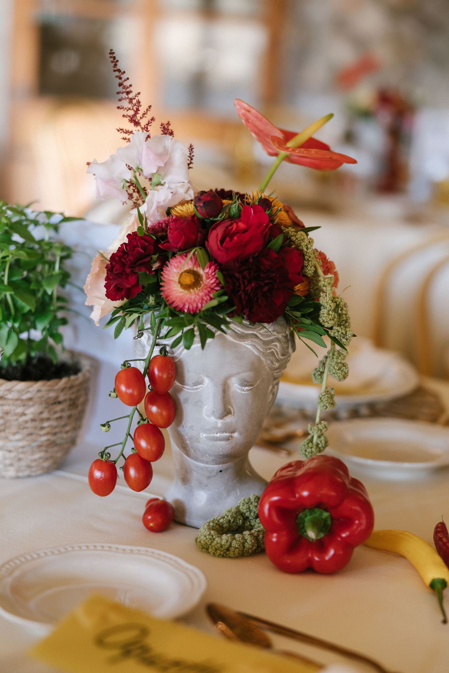 Unique Greek bust vase with red flowers, cherry tomatoes, and red pepper on wedding table.