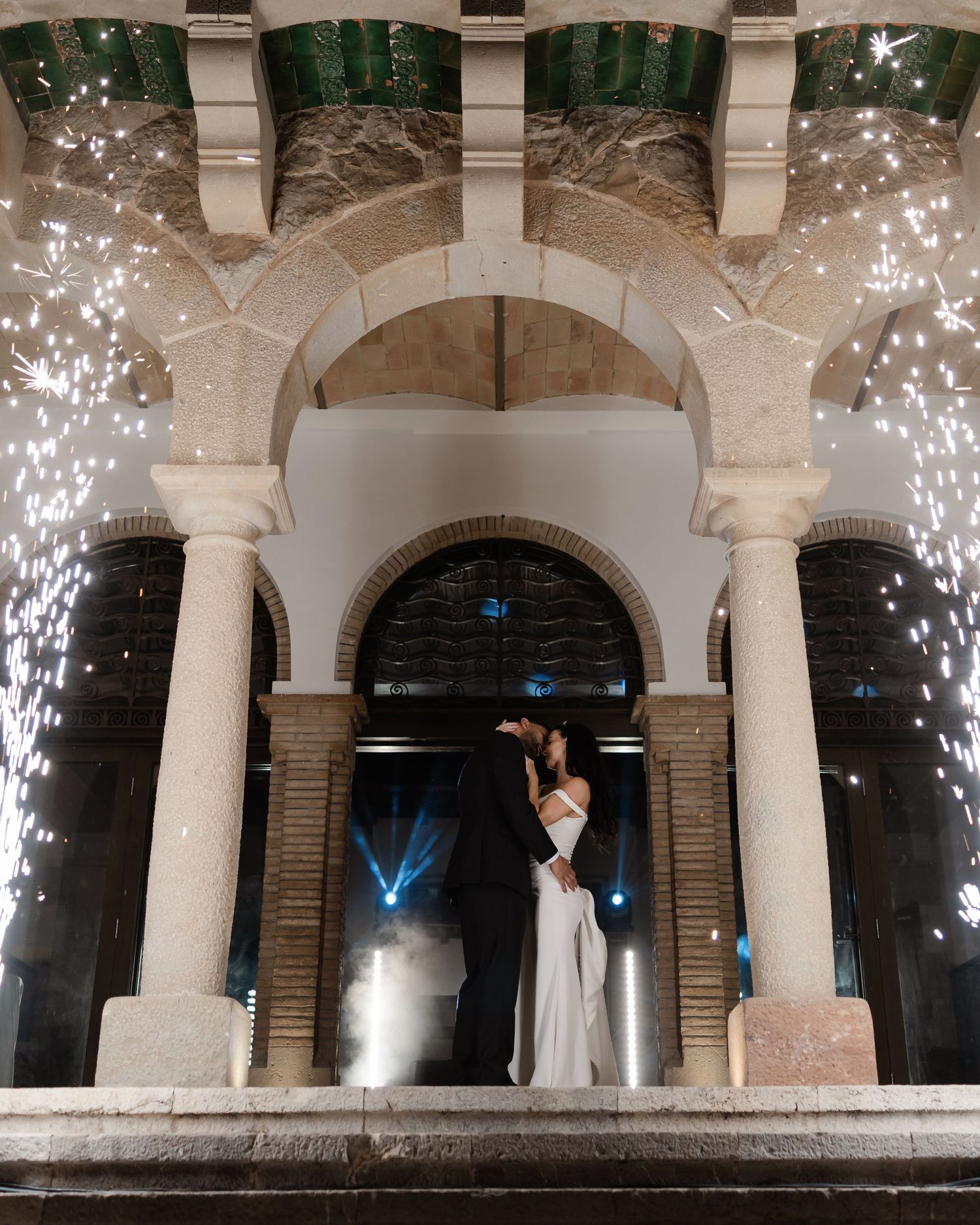 Couple kissing under stone archway with sparkling fireworks at night wedding.