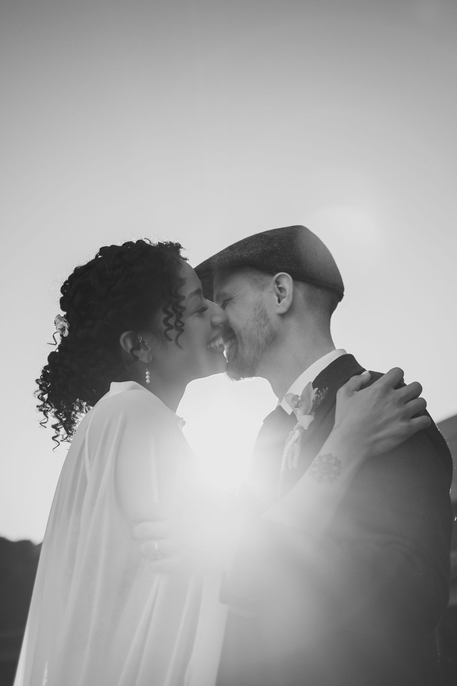 Joyful interracial couple sharing romantic moment backlit by golden sun in black and white.
