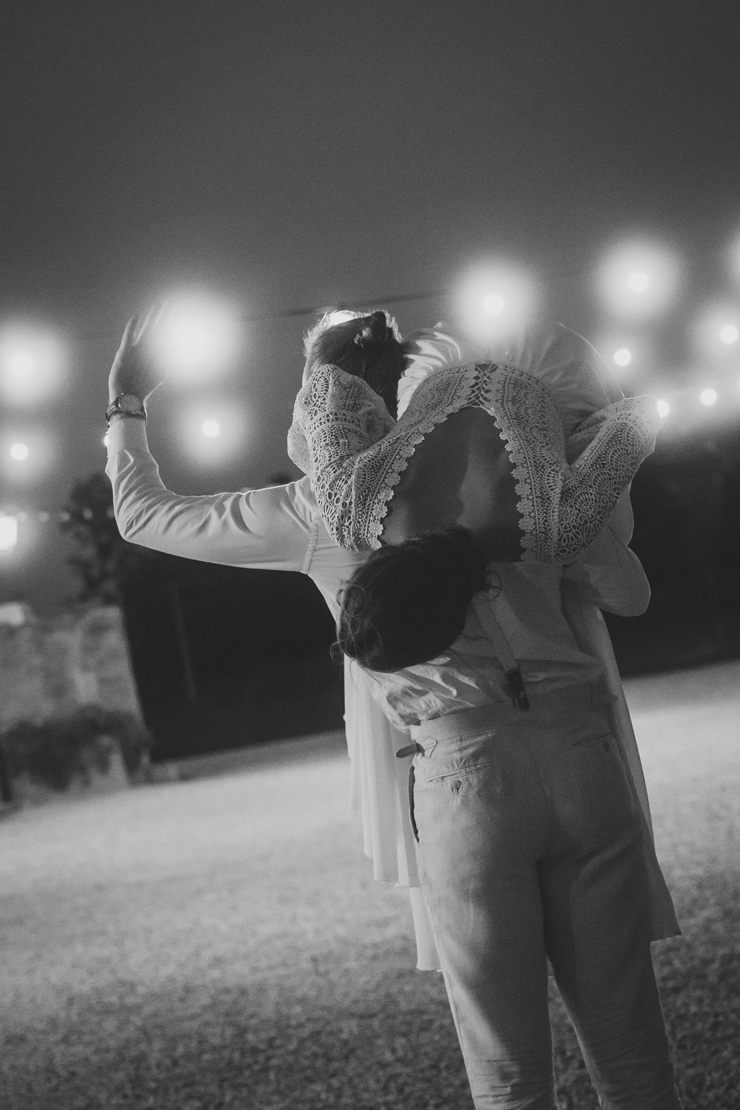 Black and white photo of couple dancing under string lights at an outdoor evening wedding reception.
