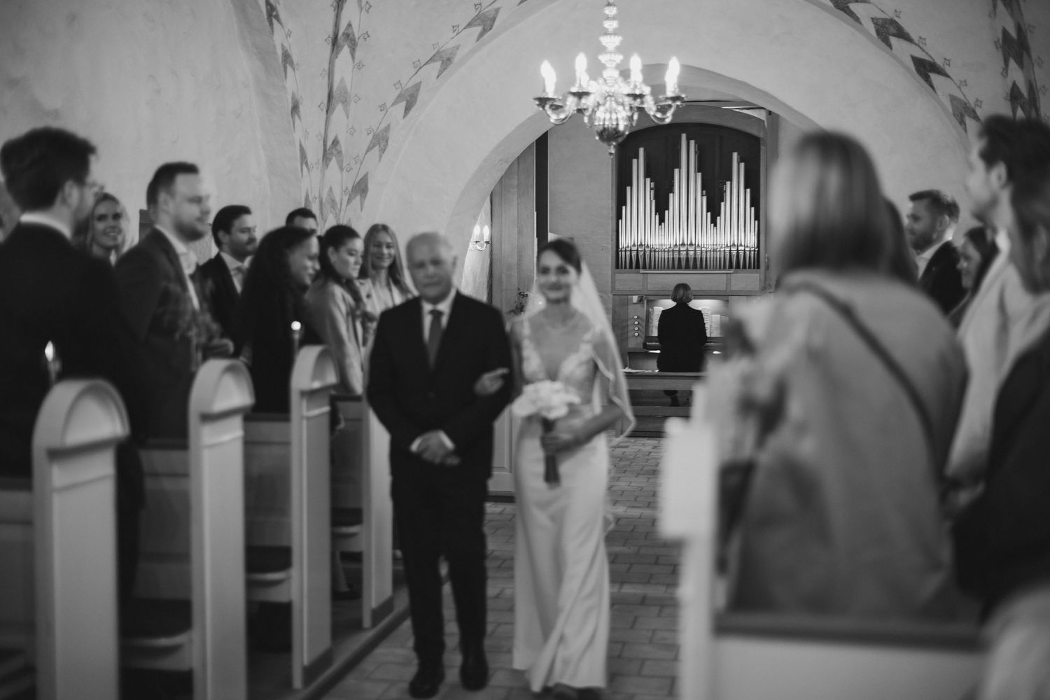 Black and white photo of a bride walking down the church aisle with her father during a wedding ceremony.