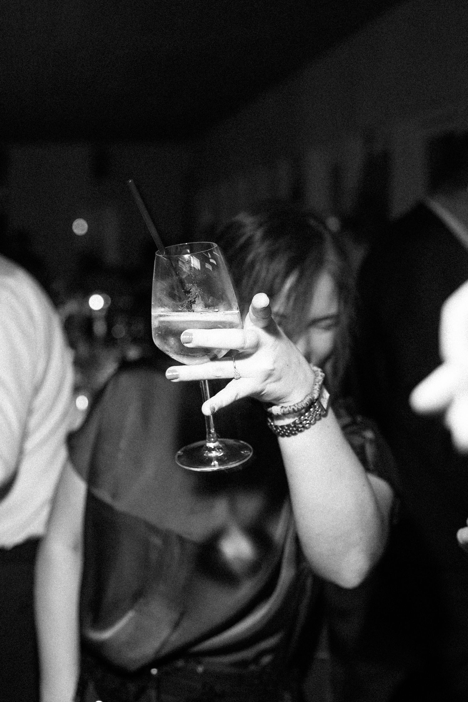 Black and white photo of wedding guest holding wine glass up at a lively reception party.
