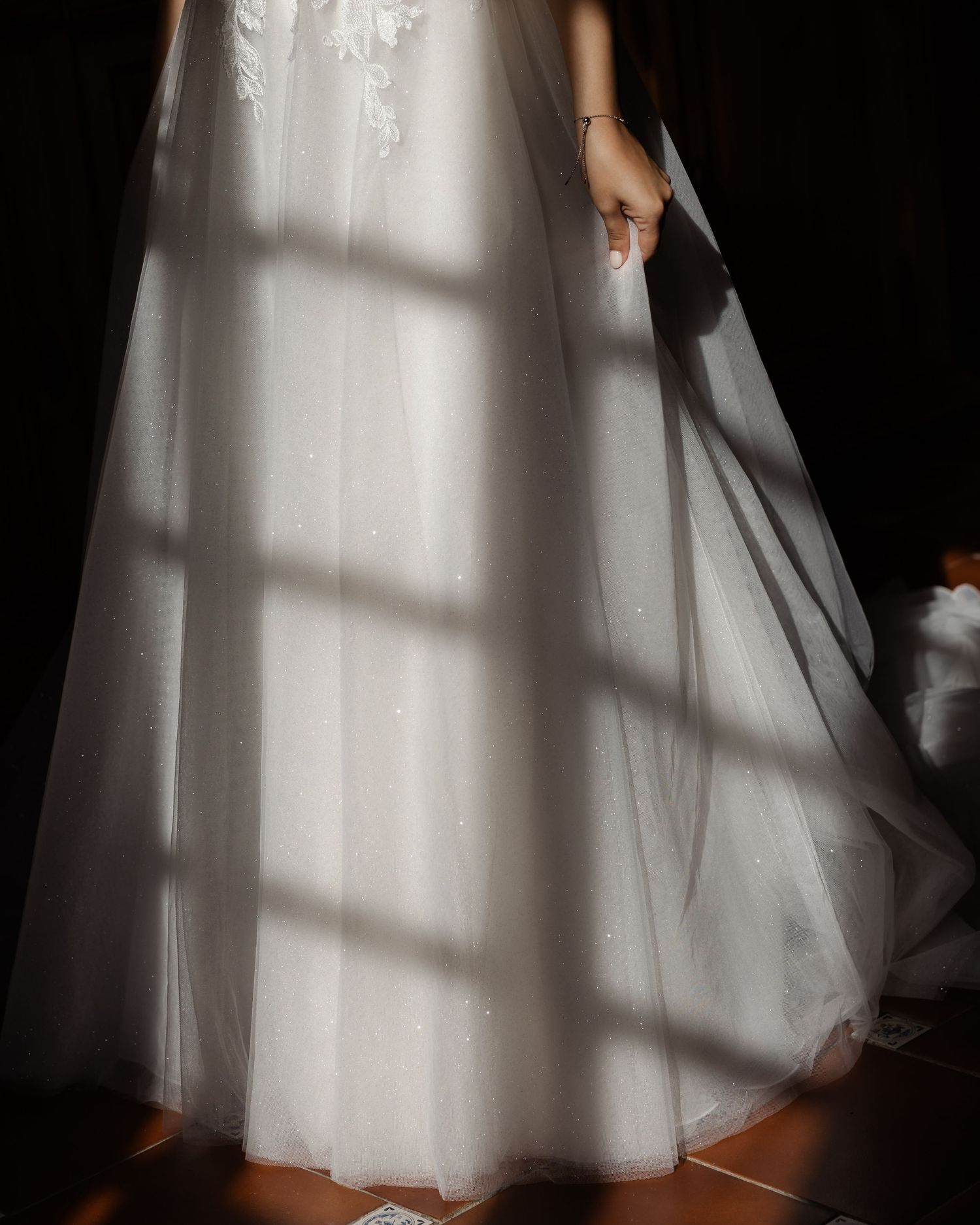 Bride in white tulle wedding gown standing in dramatic window light and shadow pattern.