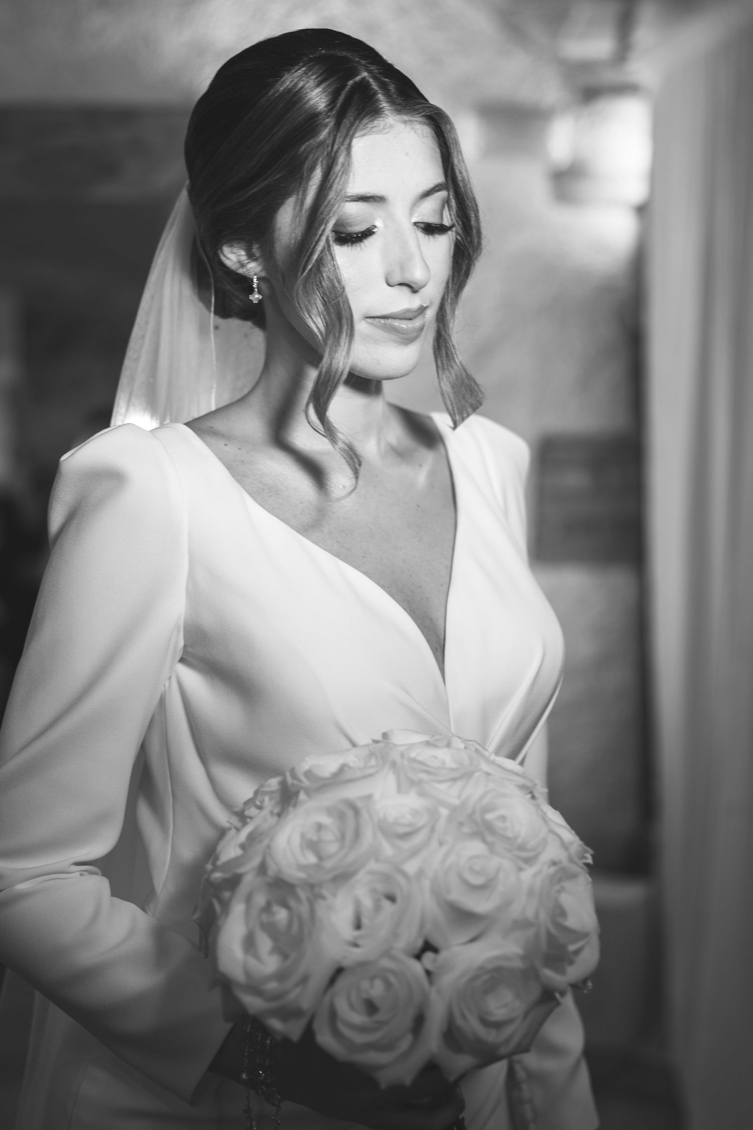 Black and white portrait of bride in white gown holding rose bouquet with eyes downcast.