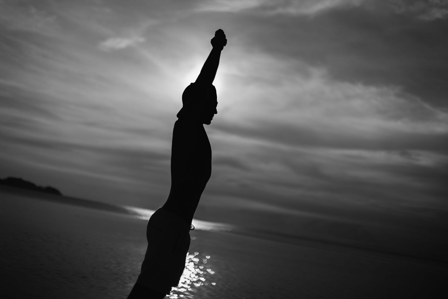 Silhouette of person raising fist against sunset sky.