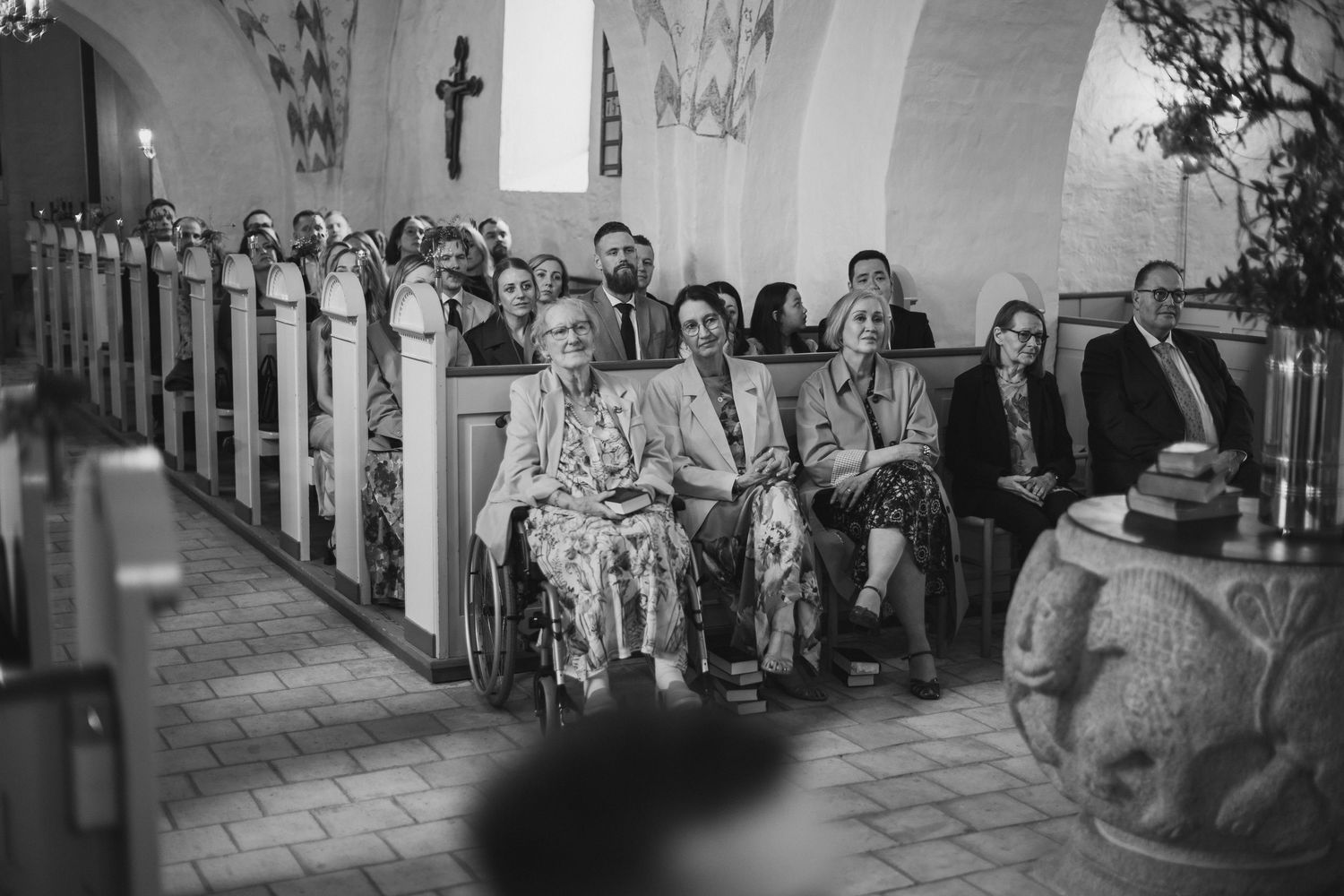Wedding guests seated in historic church pews during a ceremony, captured in black and white photography.
