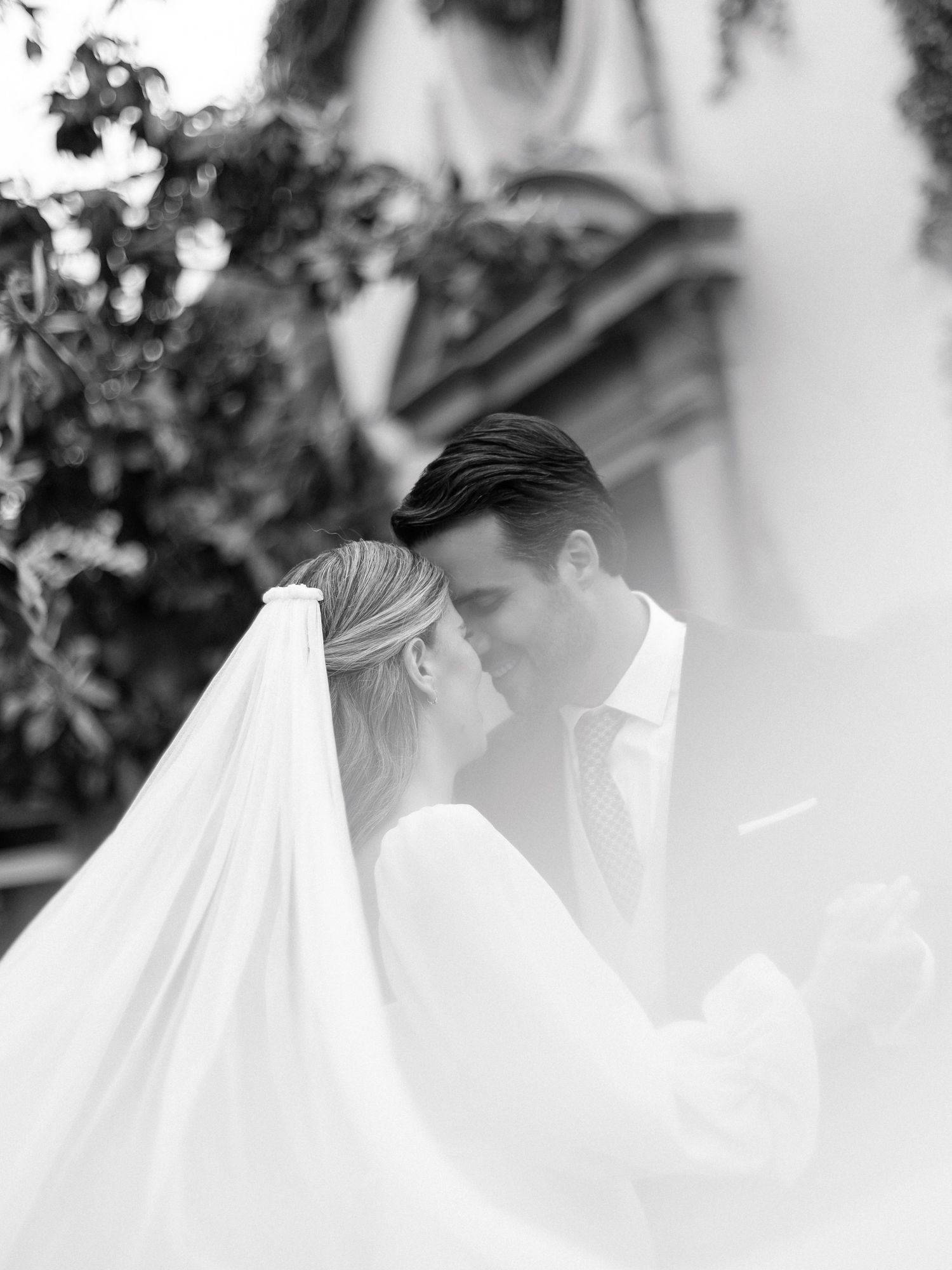 Romantic black and white photo of bride and groom sharing an intimate moment beneath a flowing veil.