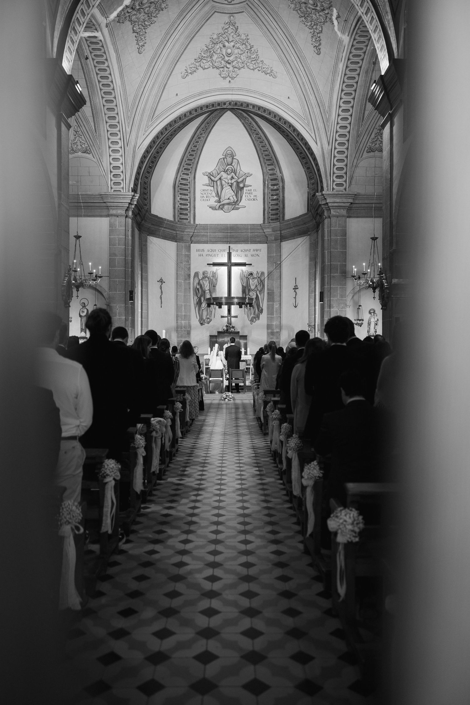 Black and white interior view of a church ceremony with guests seated in pews facing the altar.