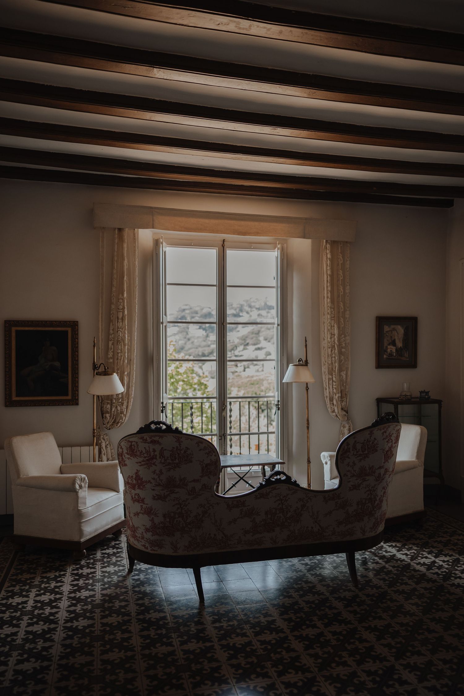 Elegant vintage room with ornate chaise lounge, French doors, and mountain views through window.
