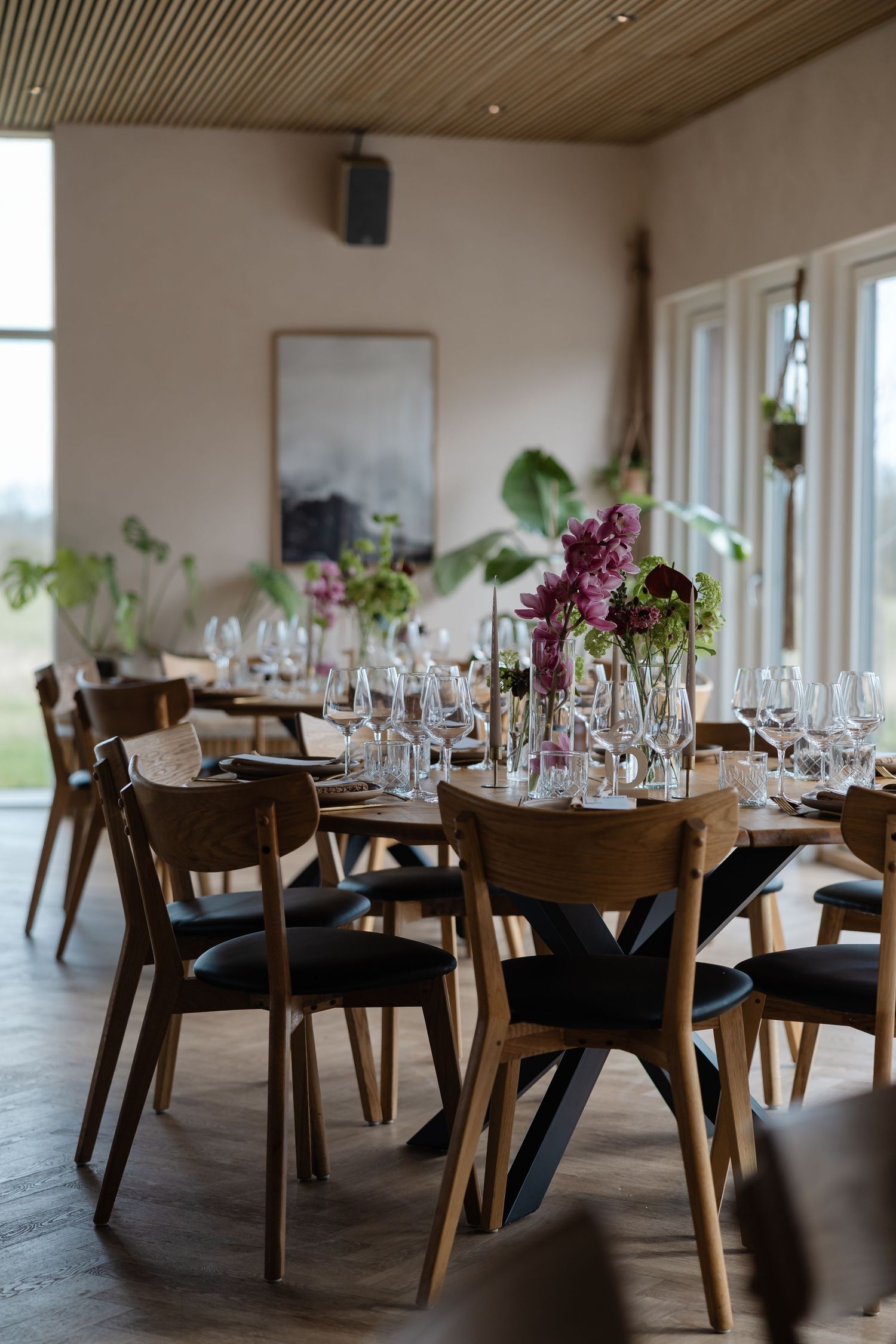 Elegant restaurant dining room with wooden chairs, set tables featuring purple floral centerpieces and wine glasses.