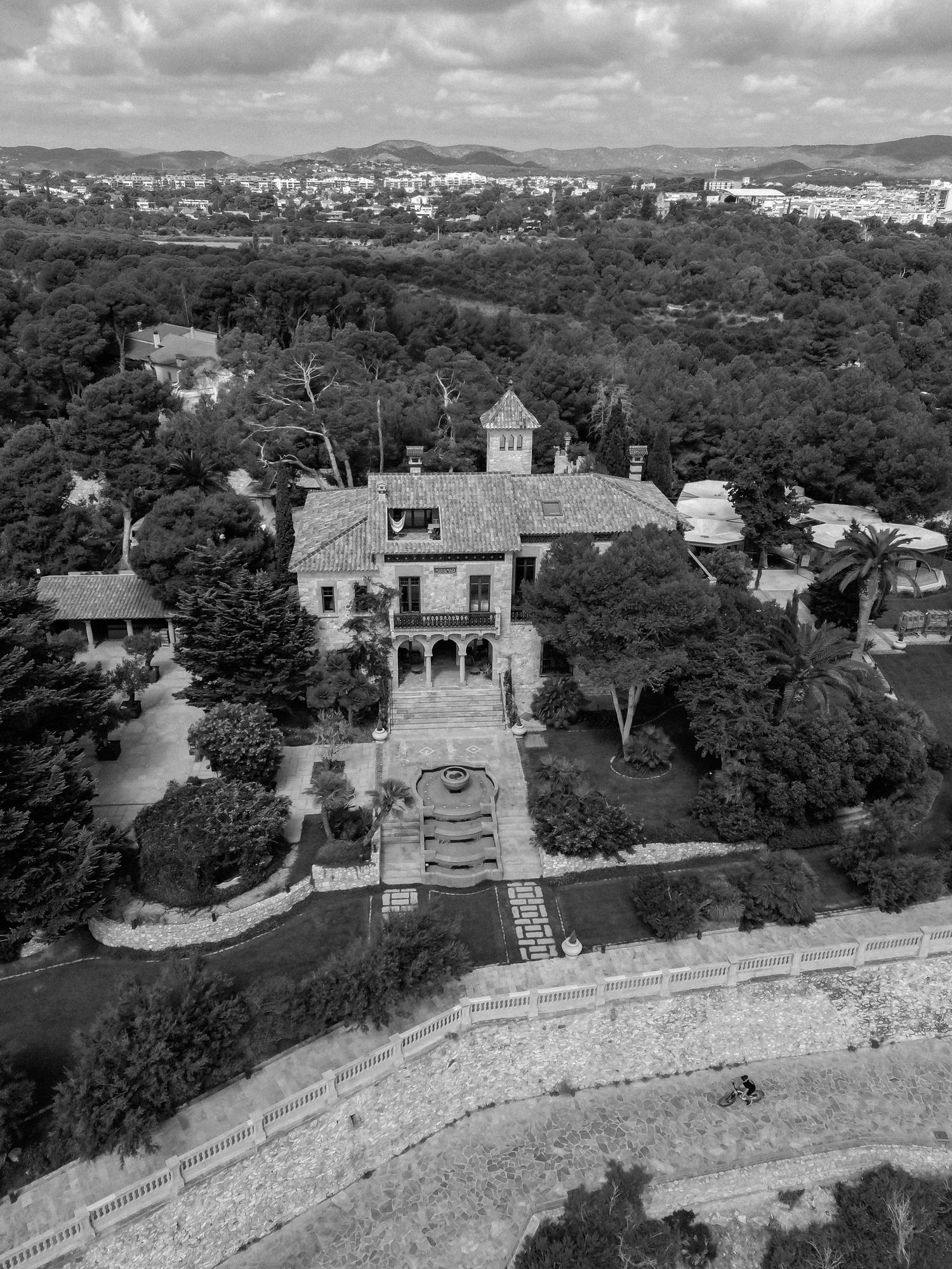 Aerial black and white view of elegant villa surrounded by lush trees and gardens.