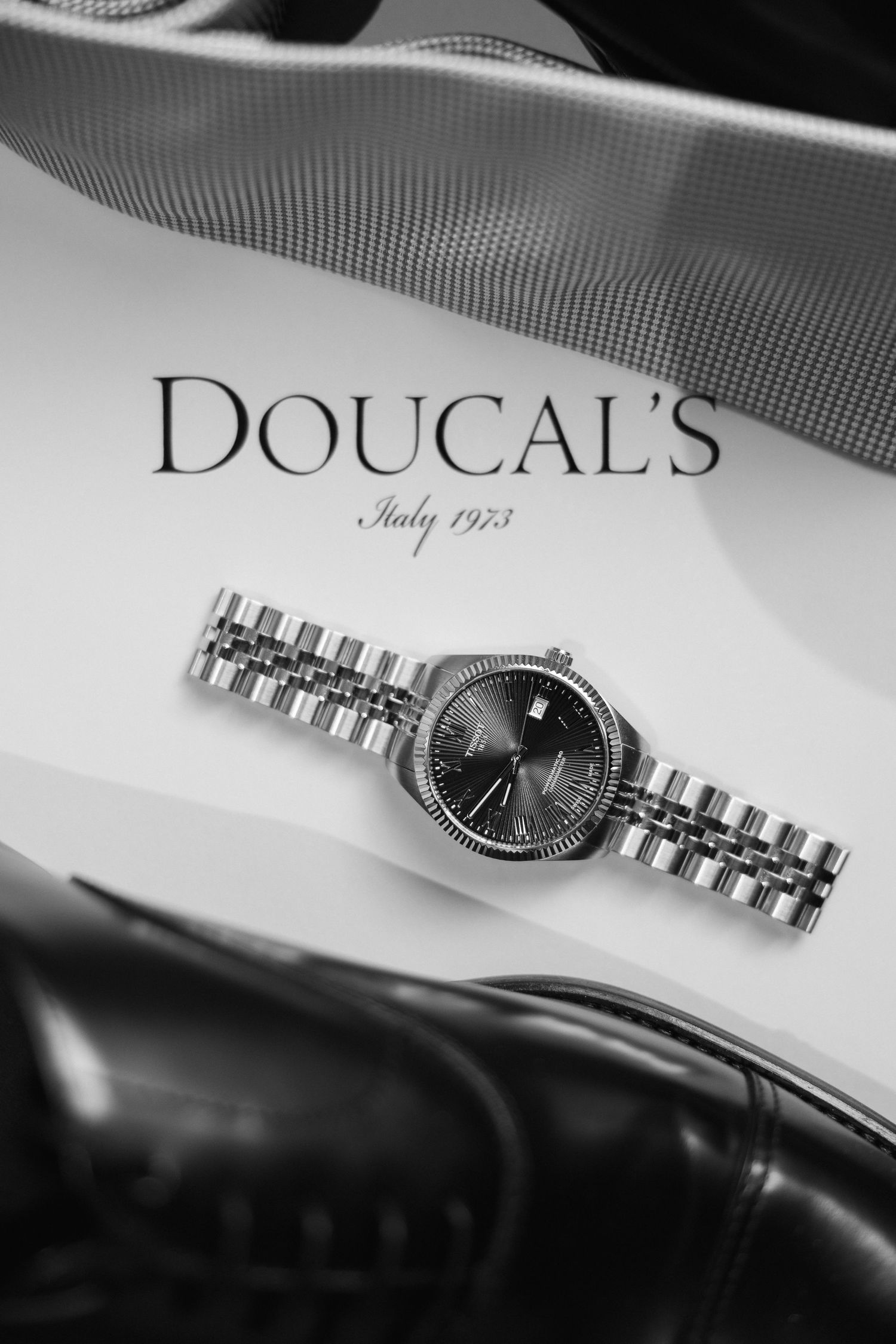 Doucal's Italy 1973 luxury silver watch displayed with black leather dress shoes in black and white photo.