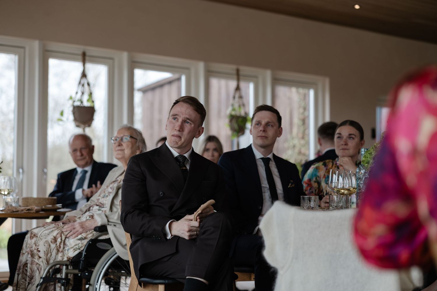 Guests in formal attire stand attentively during a wedding ceremony in an elegant venue.