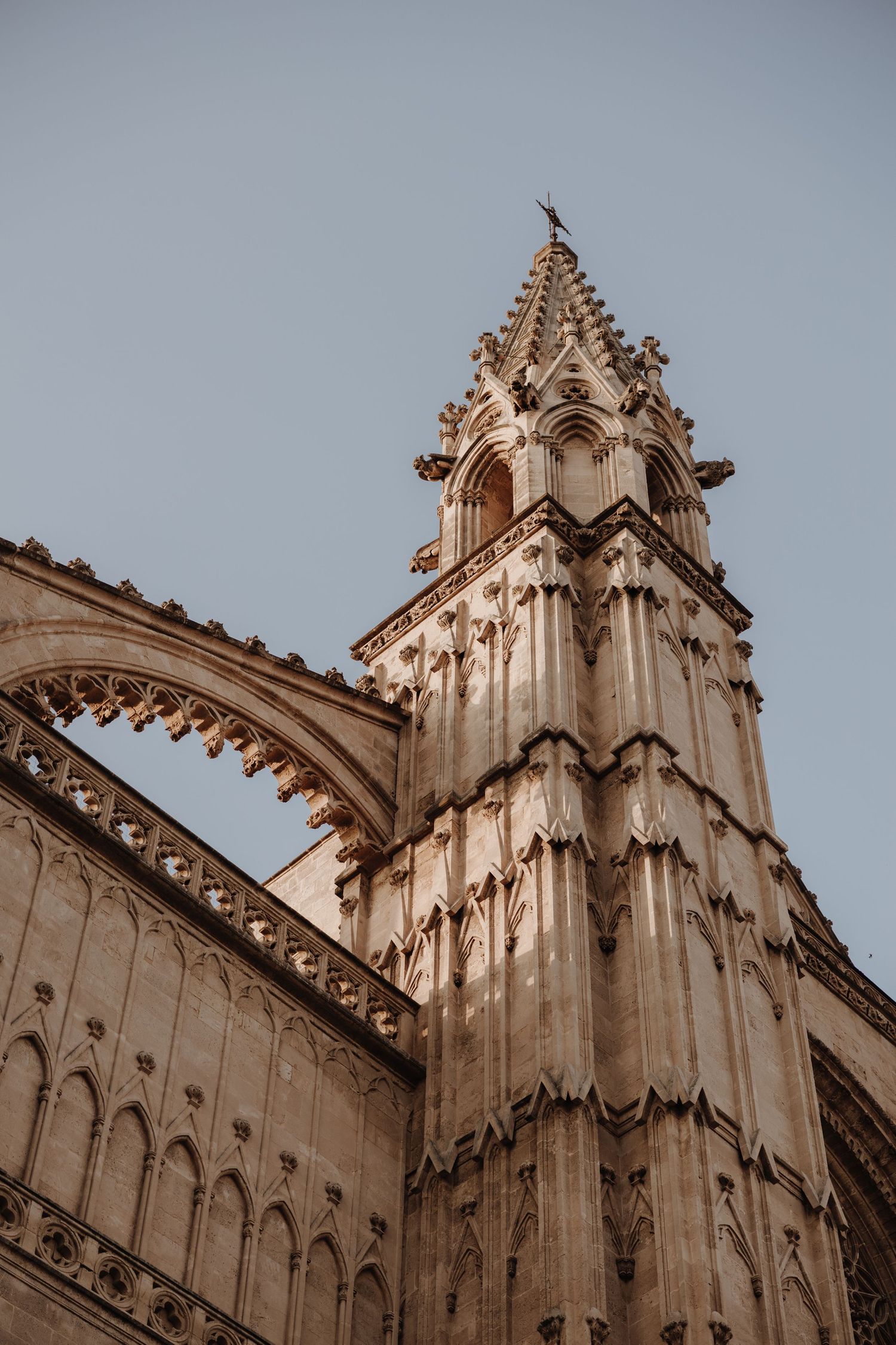 Gothic cathedral tower with ornate stone carvings and flying buttresses against a clear blue sky.