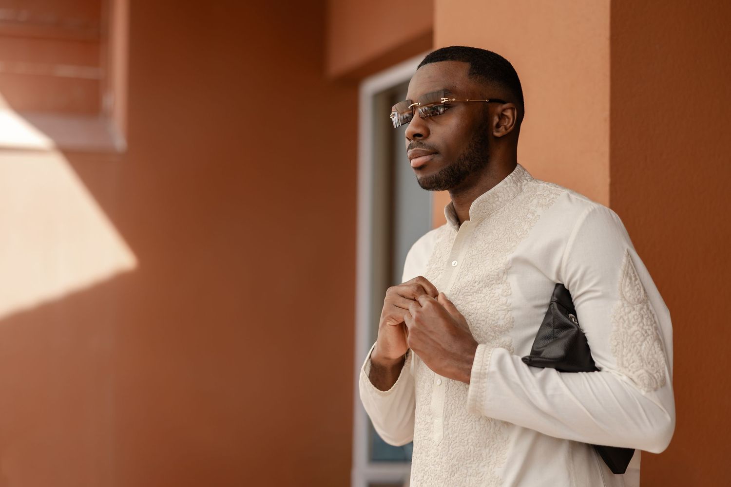 Stylish African American man in white embroidered shirt holding jacket outdoors.