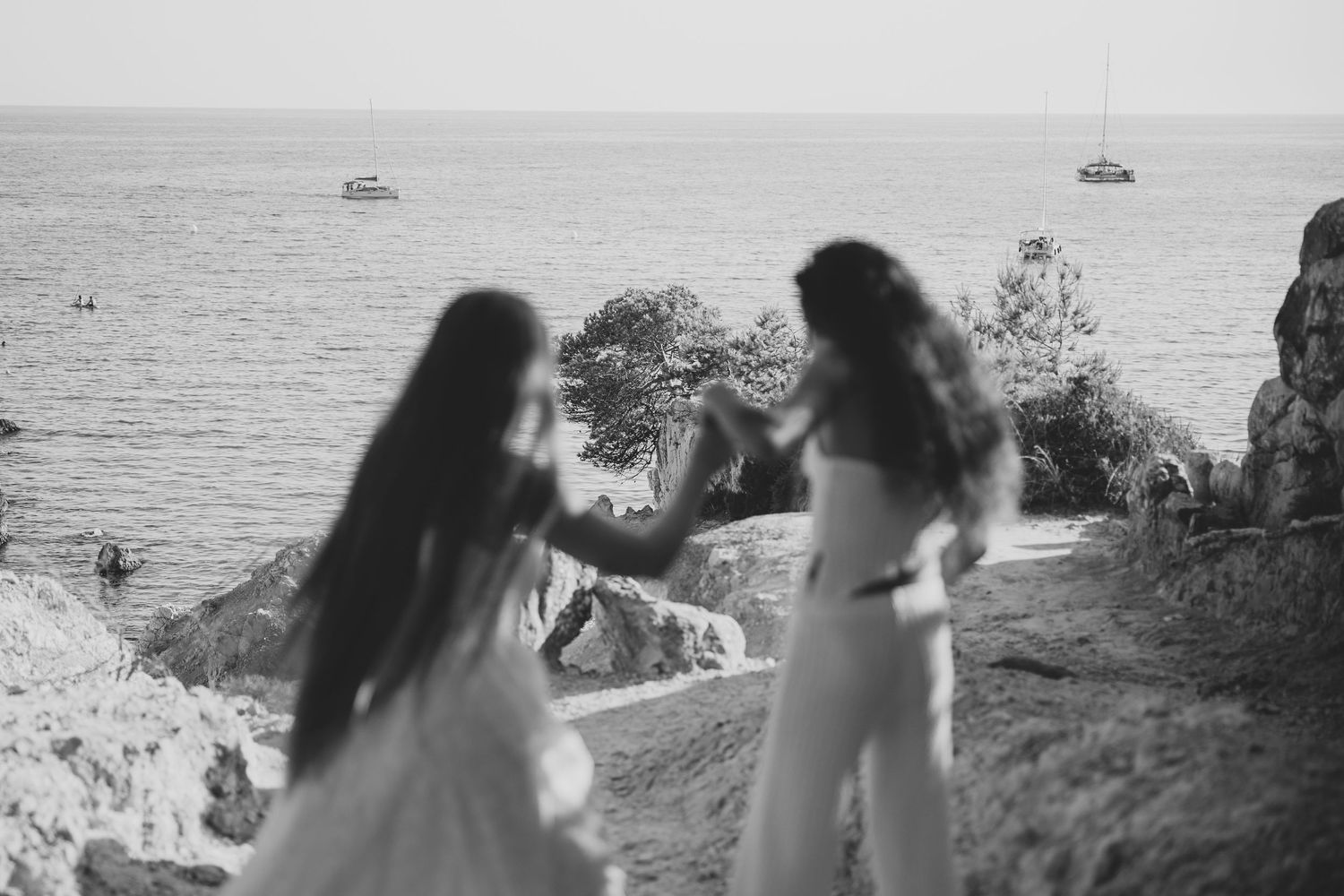 Black and white photo of two women in white standing on a cliff overlooking the ocean.