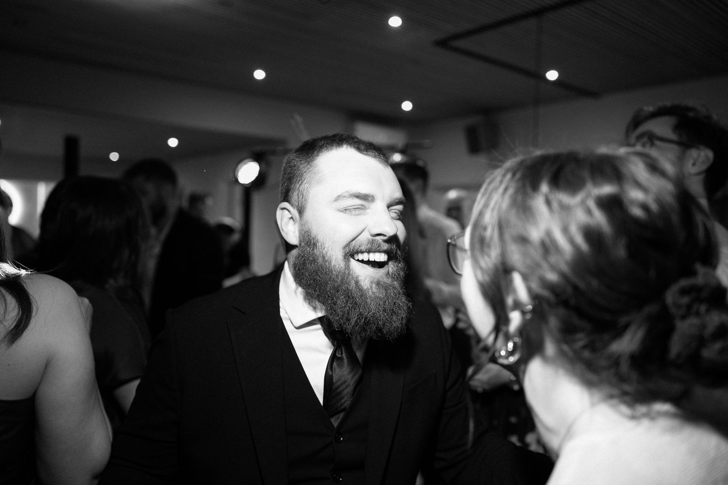 Black and white photo of bearded man laughing joyfully at a wedding reception dance floor.