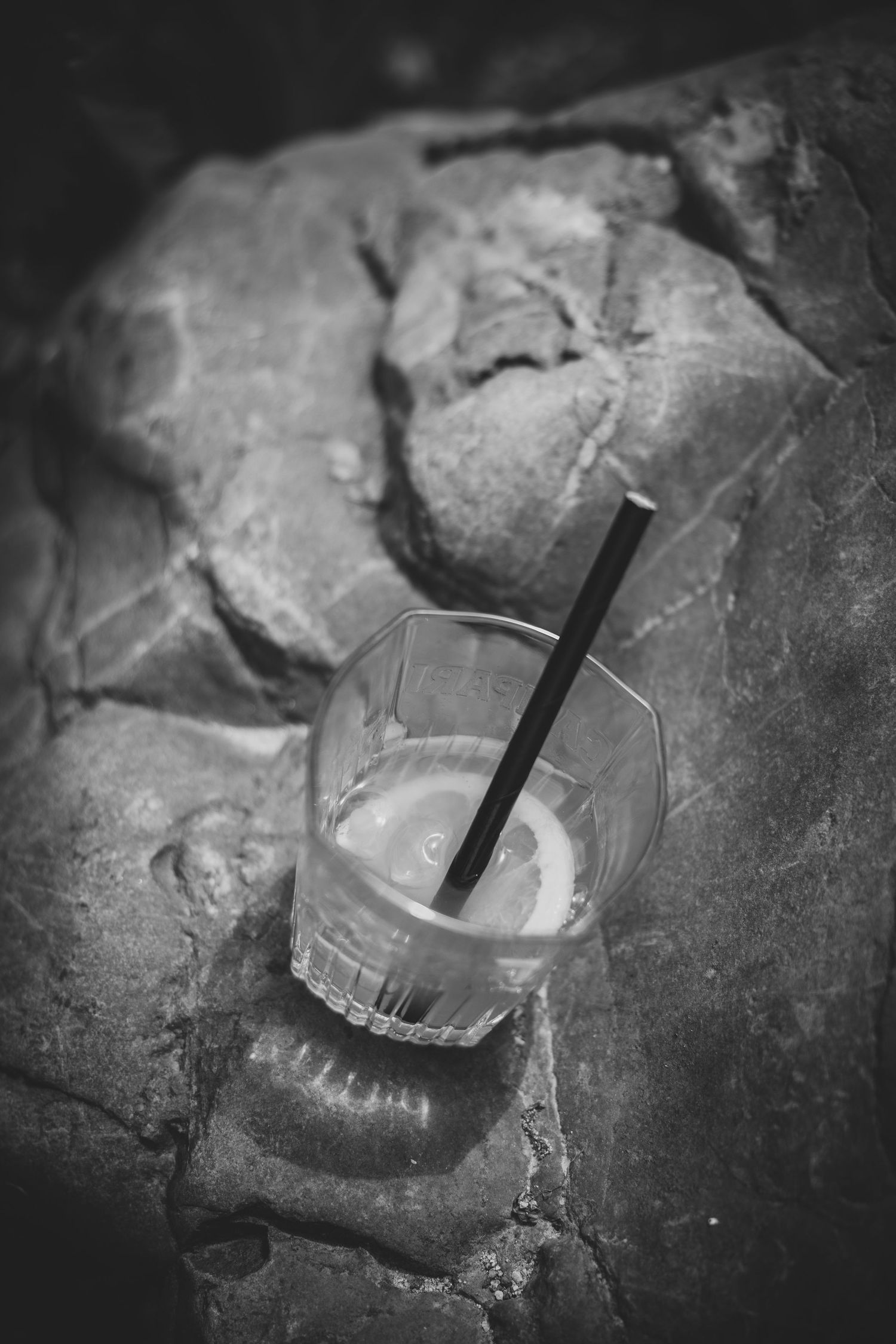 A plastic cup with a black straw resting on textured rocks, captured in black and white photography.