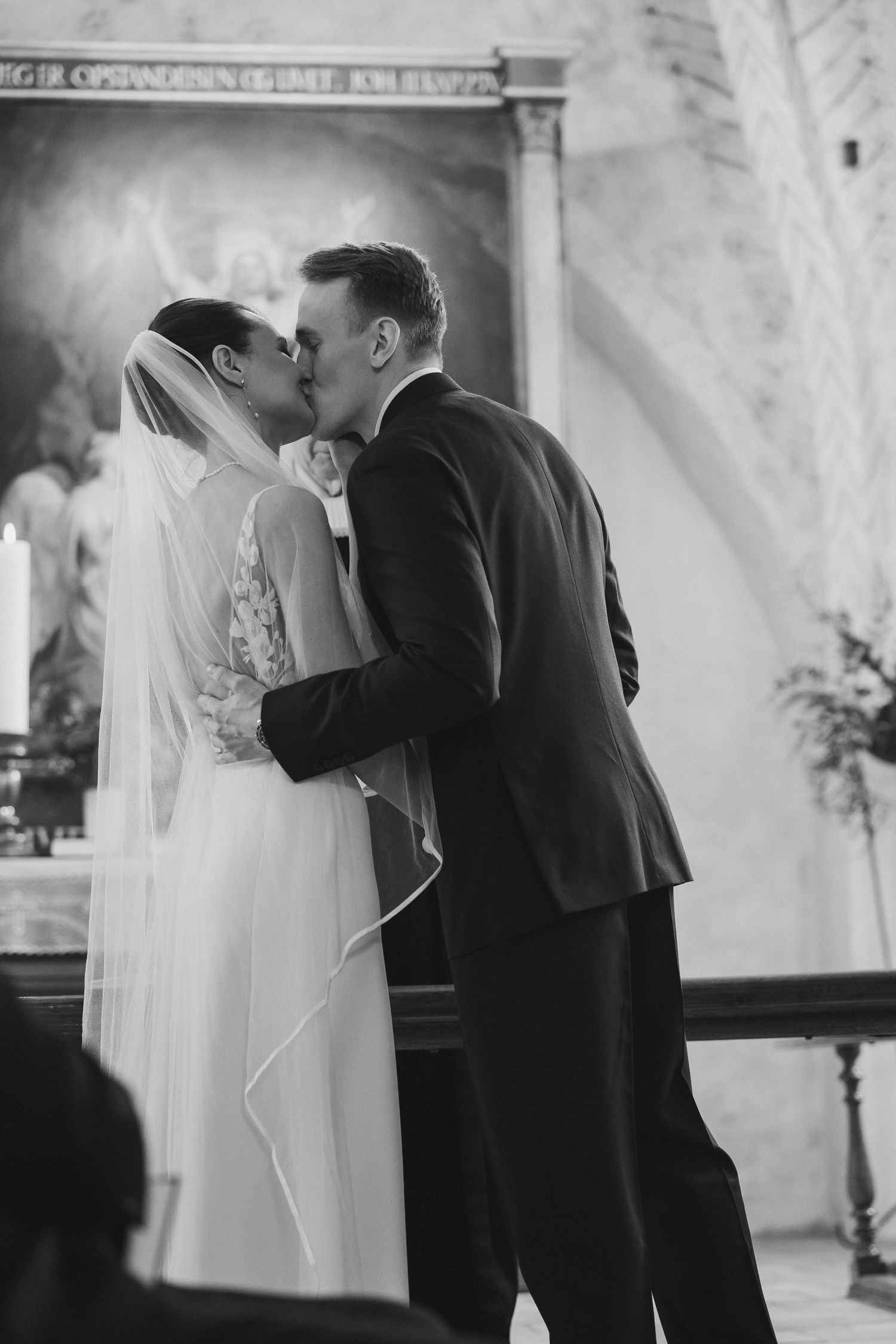 Bride and groom sharing their first kiss at the altar during a church wedding ceremony in black and white.