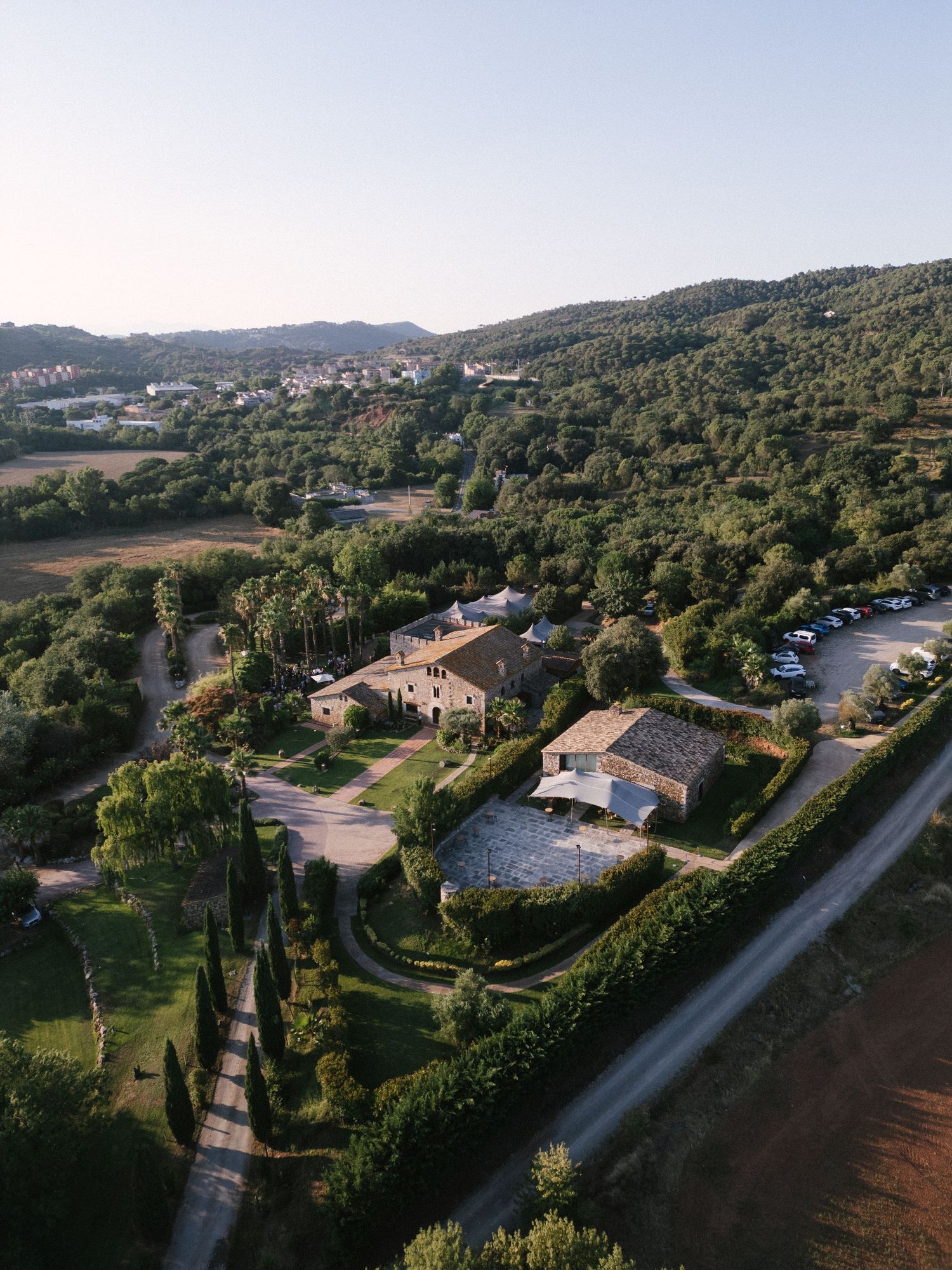 Aerial drone view of rustic stone villa estate surrounded by lush green trees and countryside.