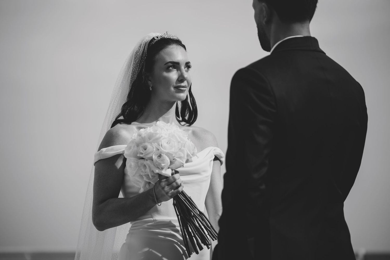Black and white photo of smiling bride holding bouquet facing groom.