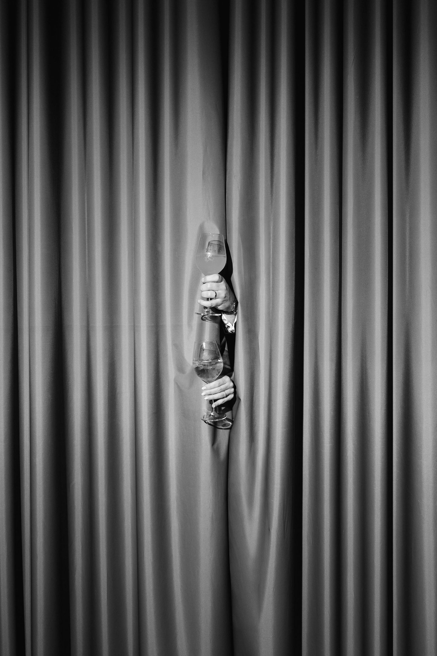 A hand emerges from stage curtains holding a microphone in a dramatic black and white theatrical photograph.