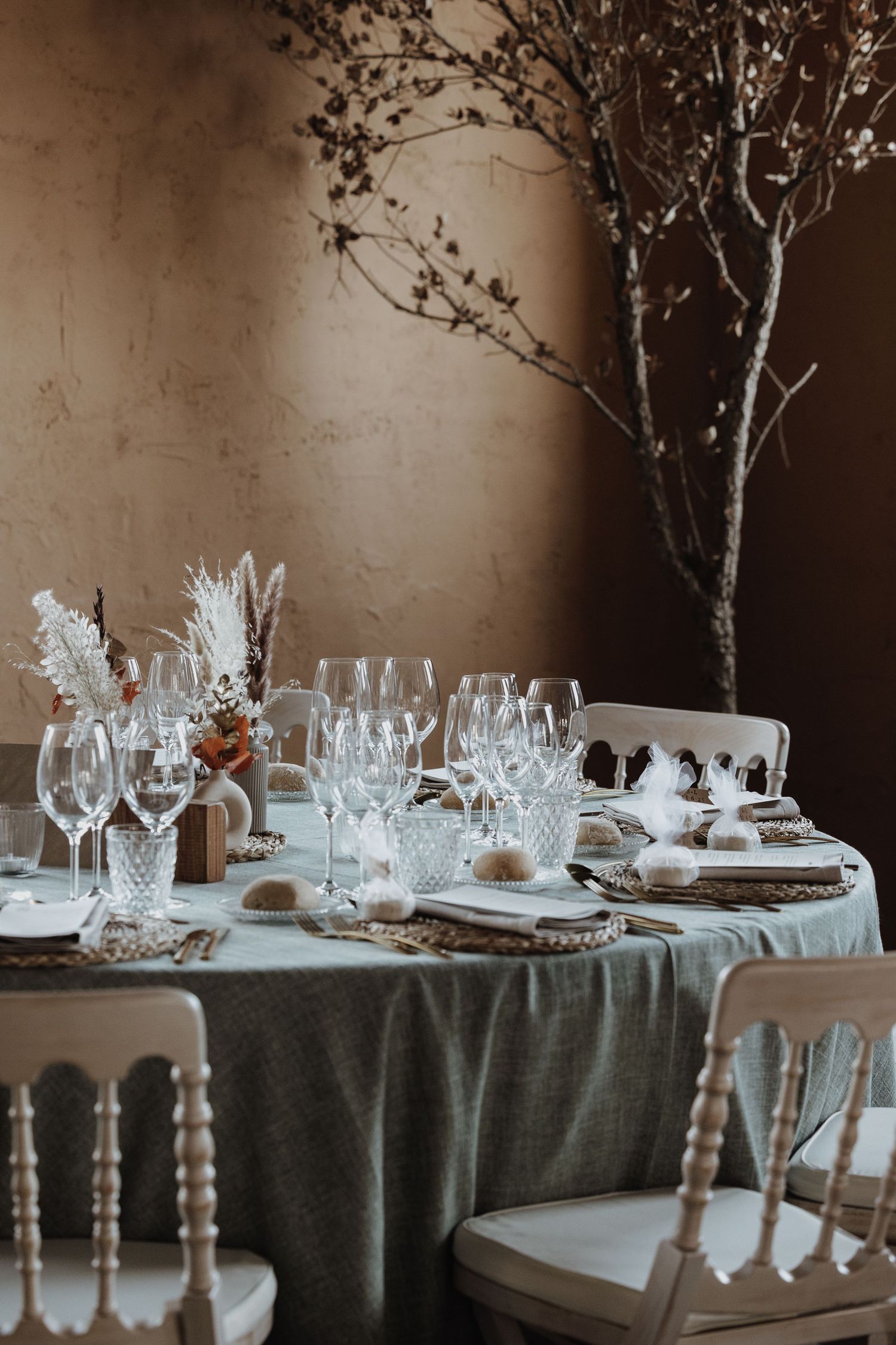 Elegant wedding tablescape with crystal glasses, dried floral arrangements, and neutral linen on round table.