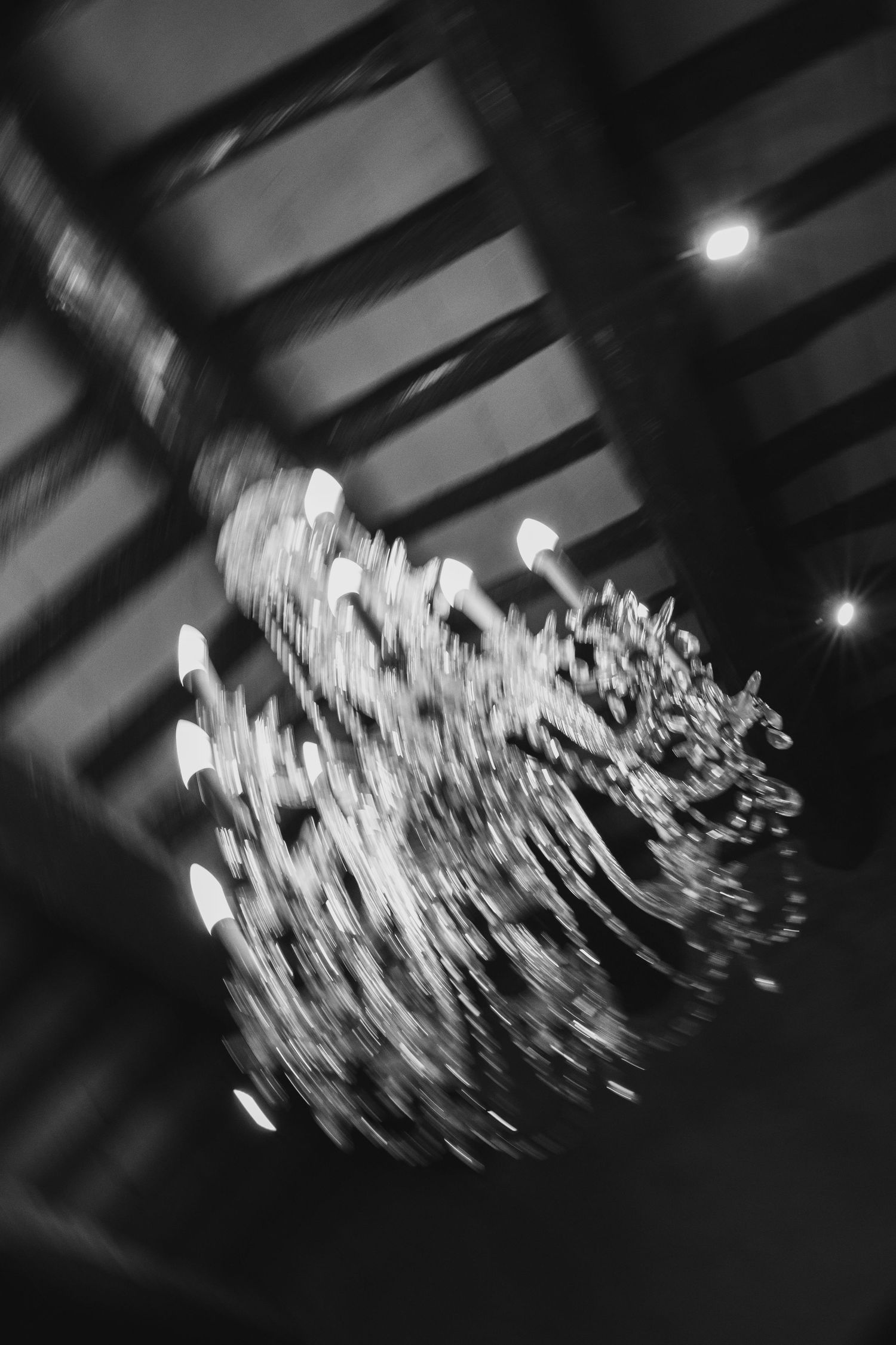 Black and white blurred chandelier hanging from wooden ceiling beams.