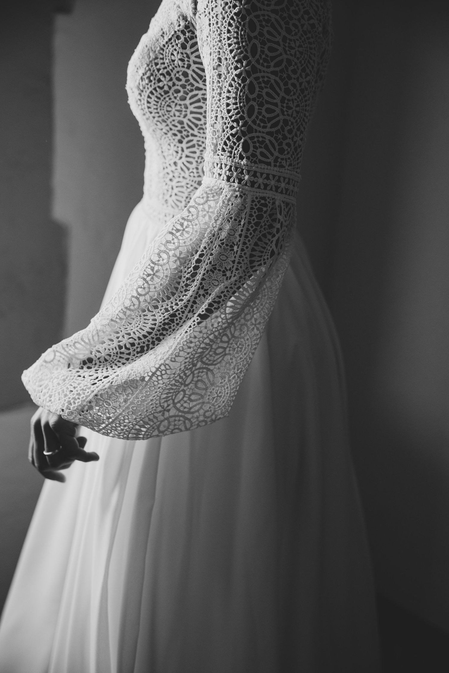 Black and white close-up of bride wearing elegant long-sleeve lace wedding dress with flowy skirt.
