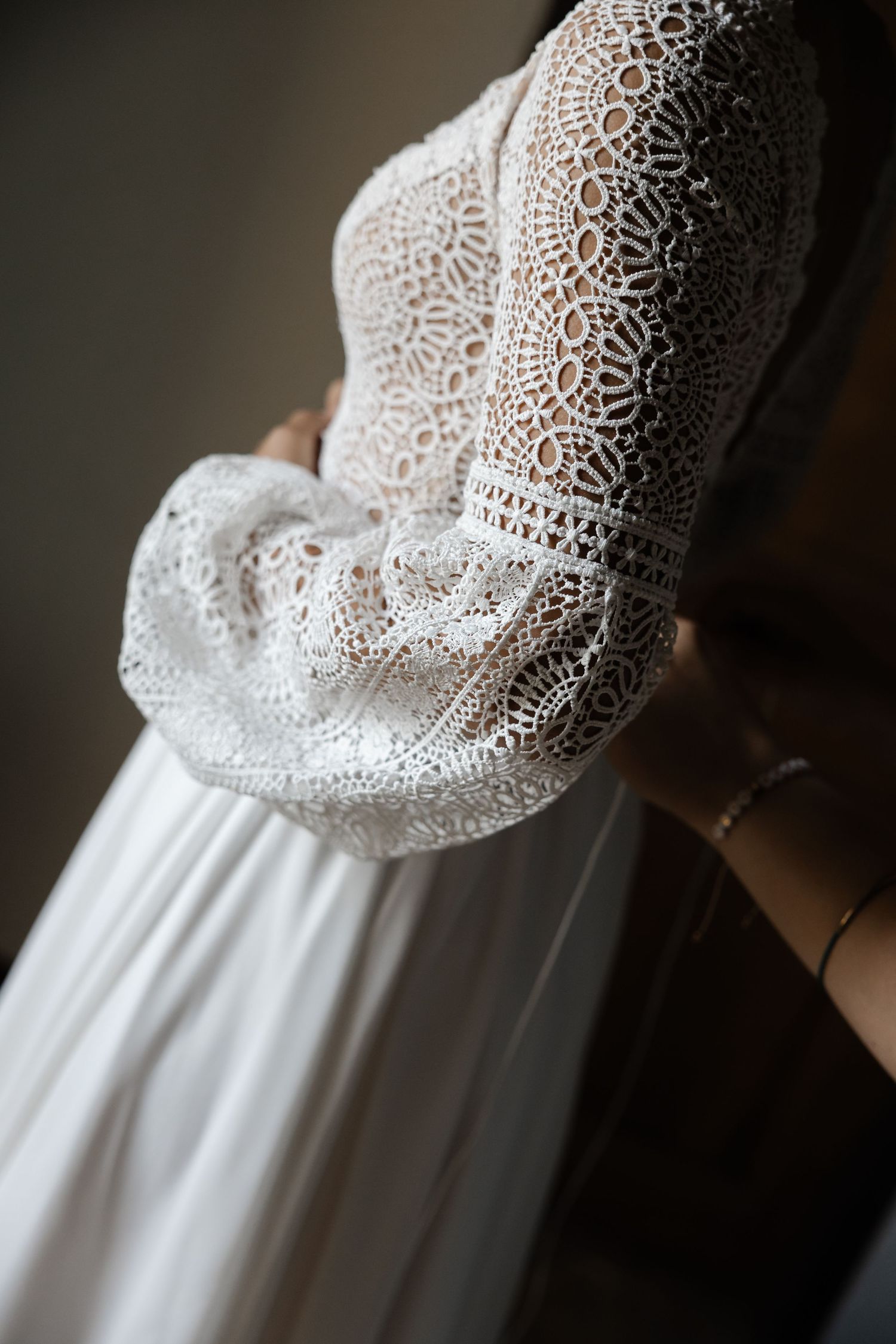 Close-up detail of a stunning white bridal gown featuring intricate crochet lace sleeves and flowing chiffon skirt.