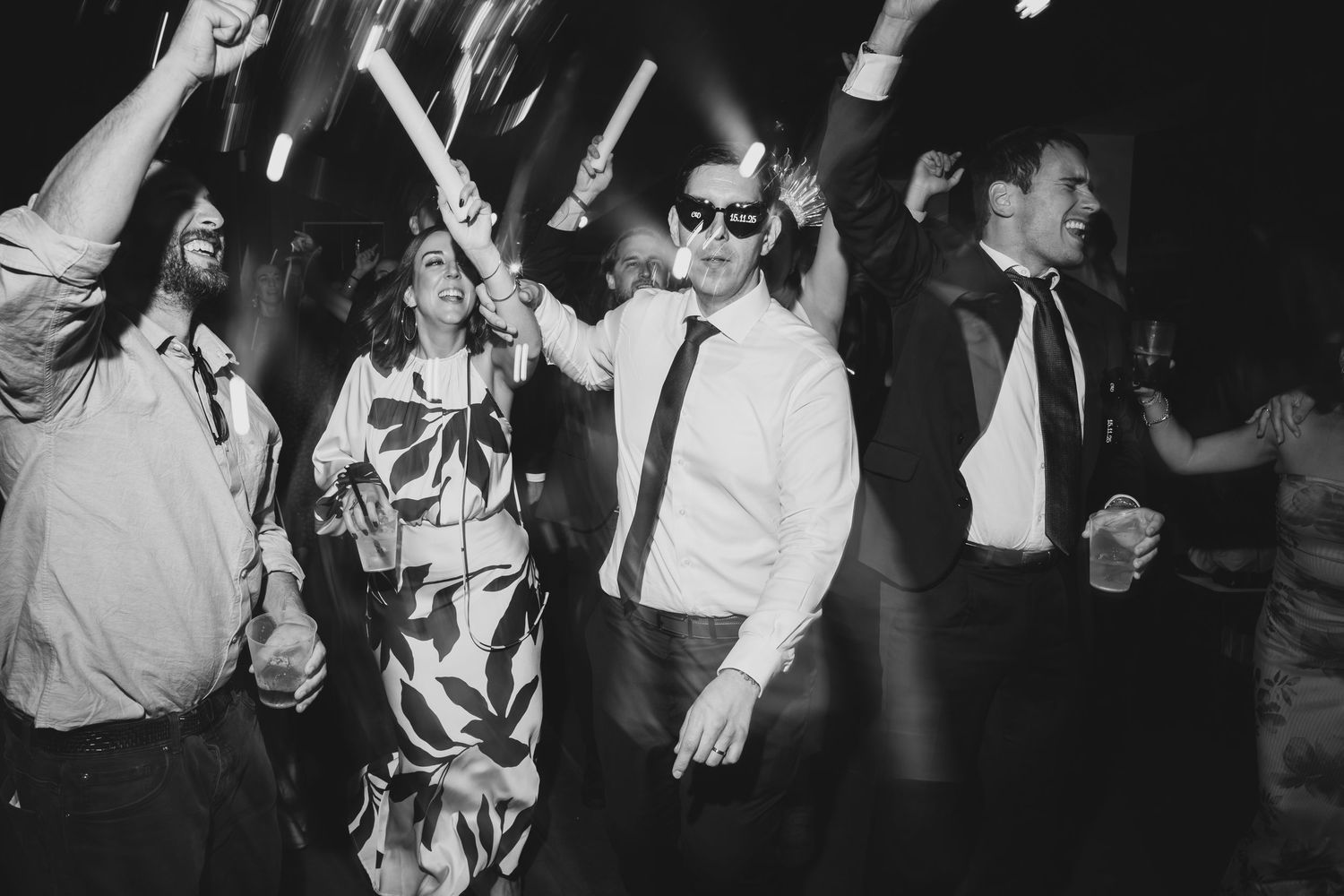 Black and white photo of wedding guests dancing energetically on the dance floor at a reception.