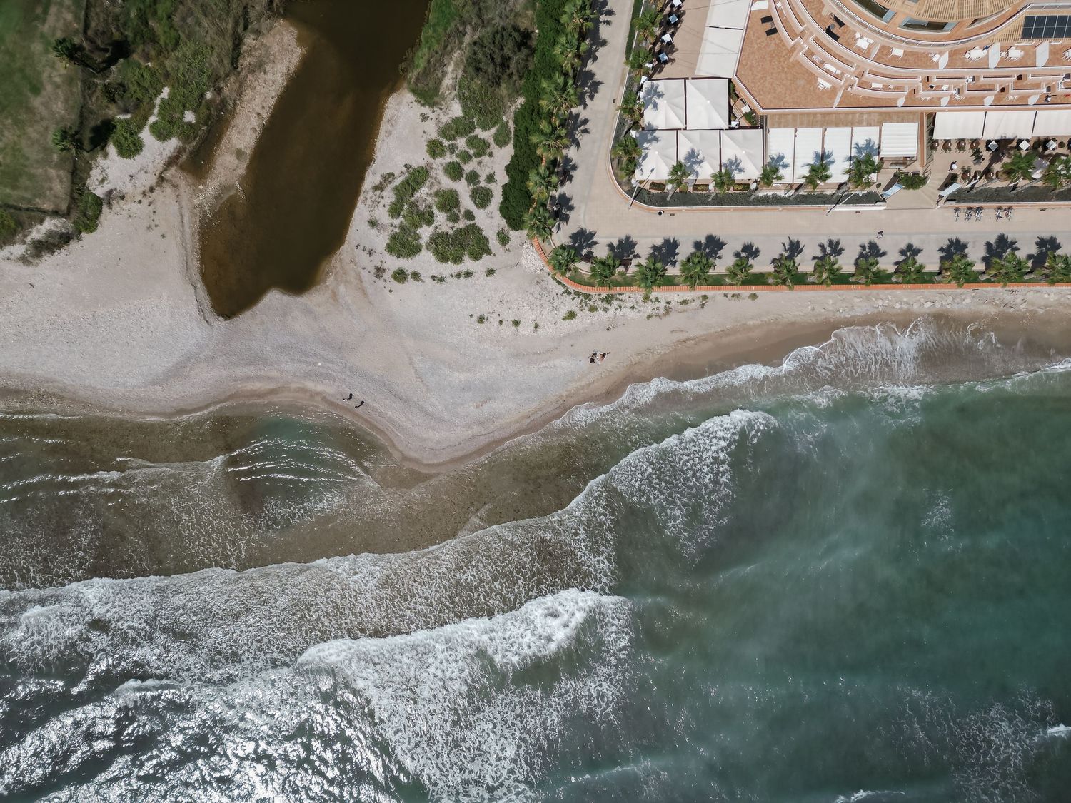 Aerial drone view of sandy beach coastline with resort property and ocean waves in daylight.
