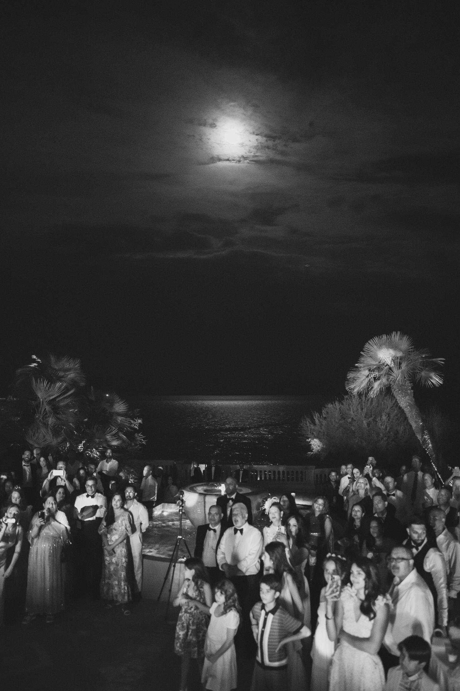 Black and white aerial view of wedding reception crowd under full moon.