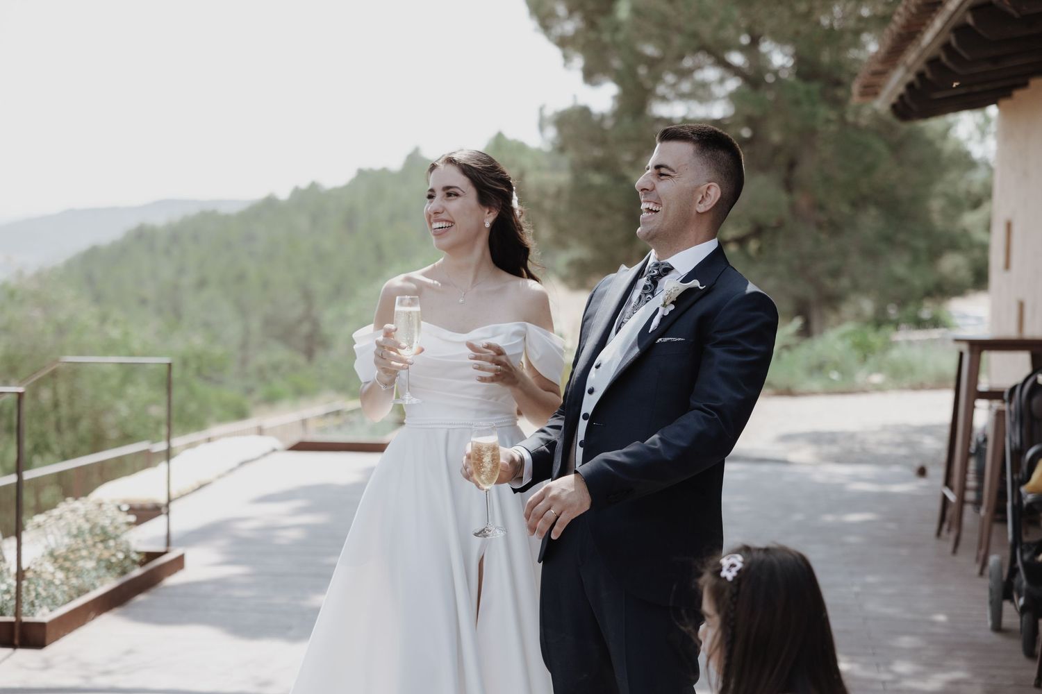 Happy bride and groom toasting with champagne glasses at an outdoor wedding venue with scenic views.