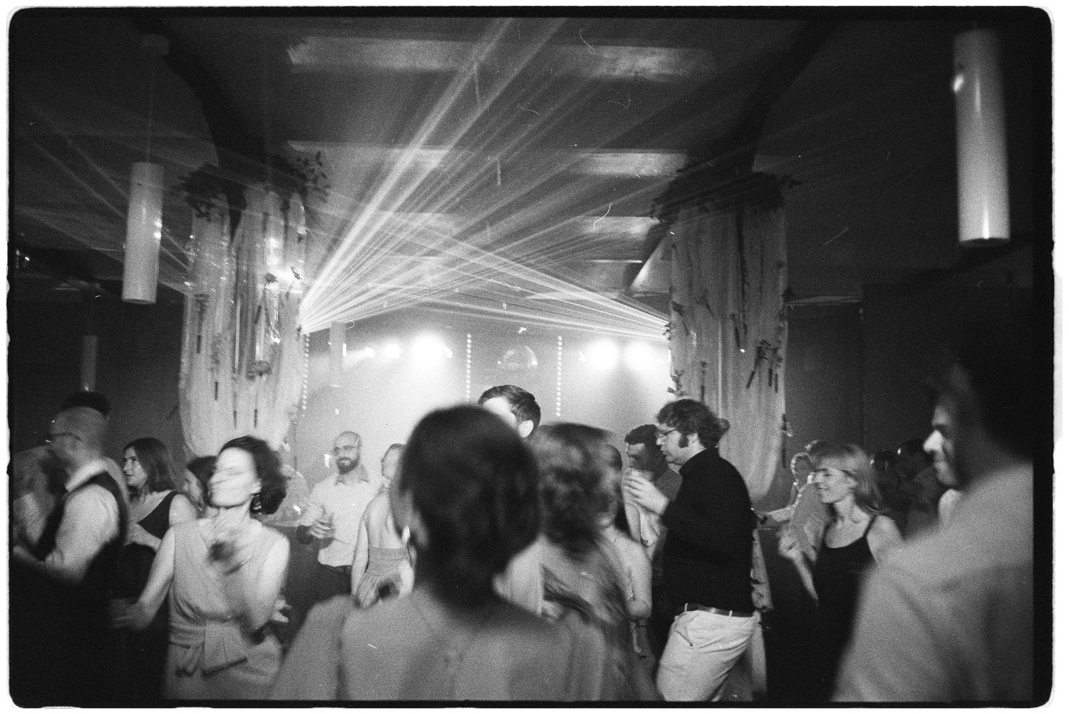Wedding guests dance under dramatic laser lights in a dark venue in a black and white photo.