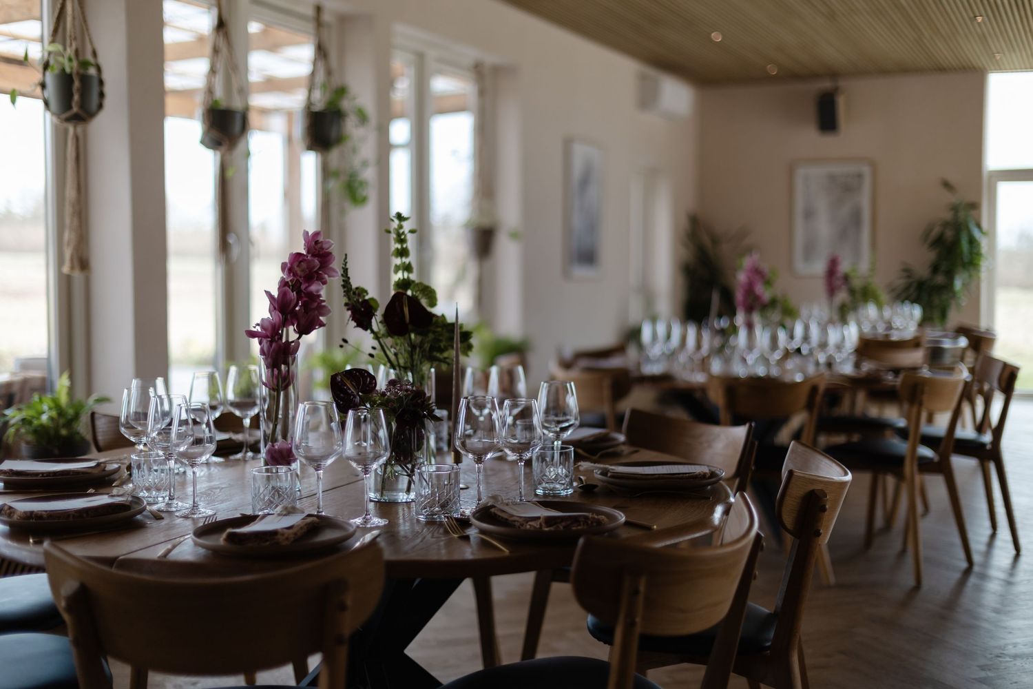 Elegant restaurant dining room with round wooden tables set with wine glasses and floral centerpieces.