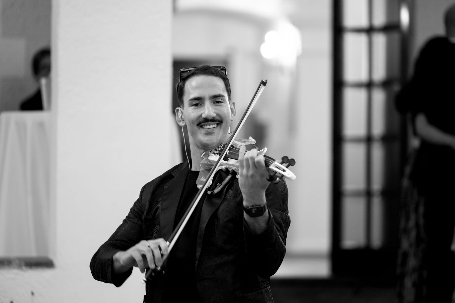 Black and white photo of a smiling violinist performing with a bow at a wedding reception.