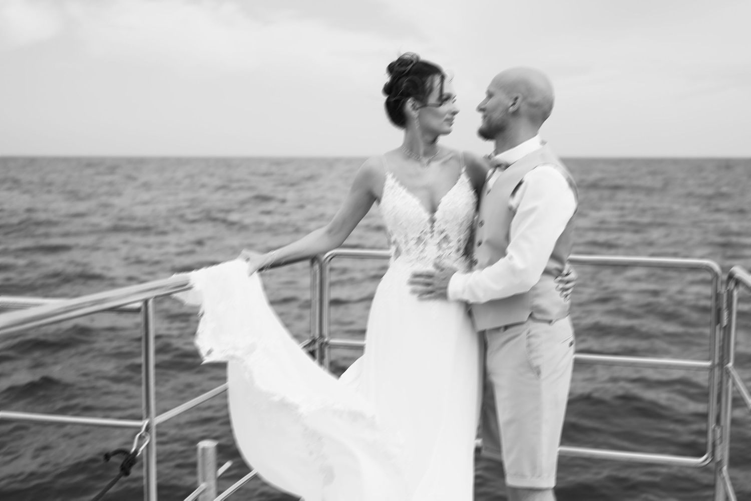 Bride and groom embrace on a yacht deck with ocean backdrop in elegant black and white wedding photo.